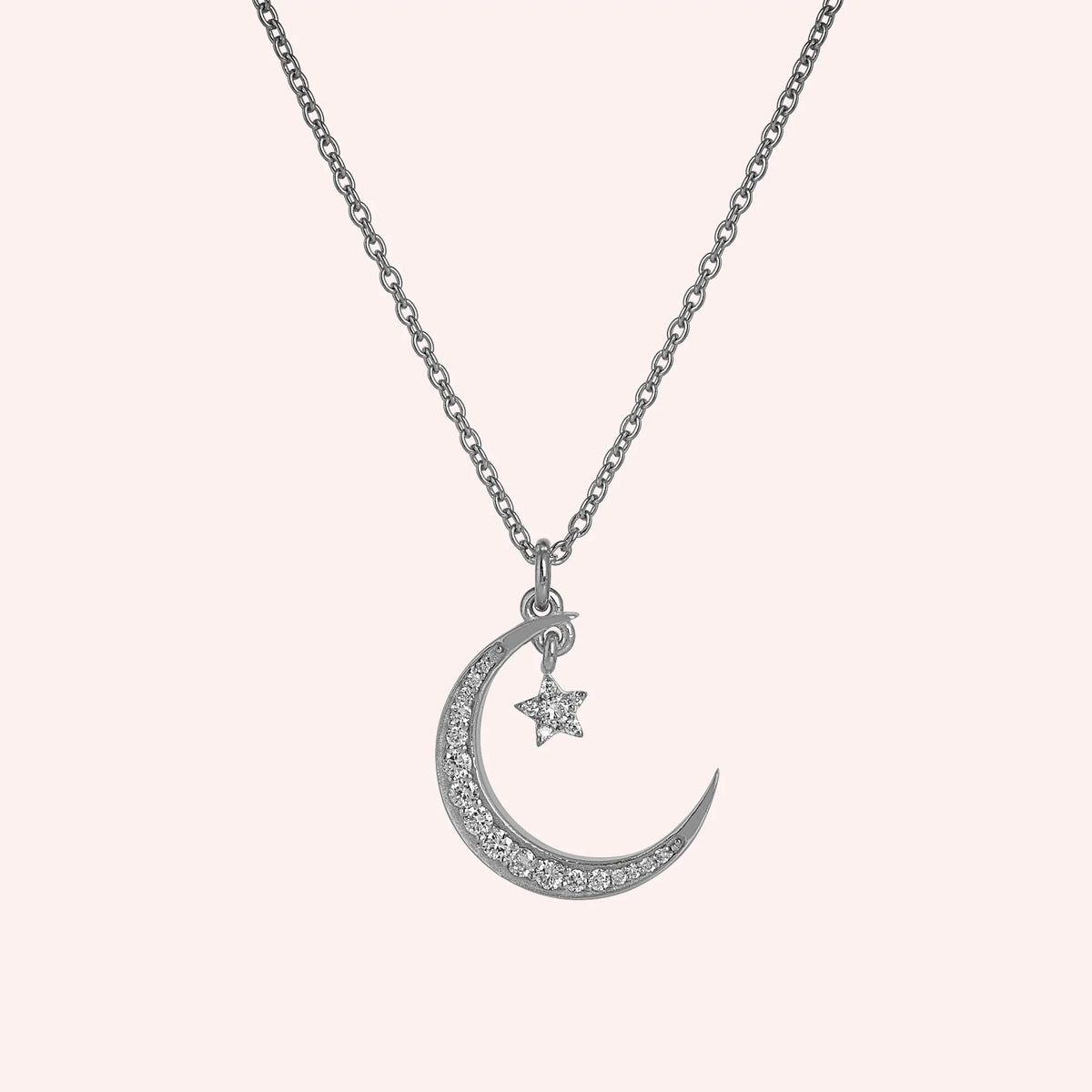 Moon_necklace_in_sterling_silver_with_a_small_star_charm_at_front_angle_view_on_solid_pink_background