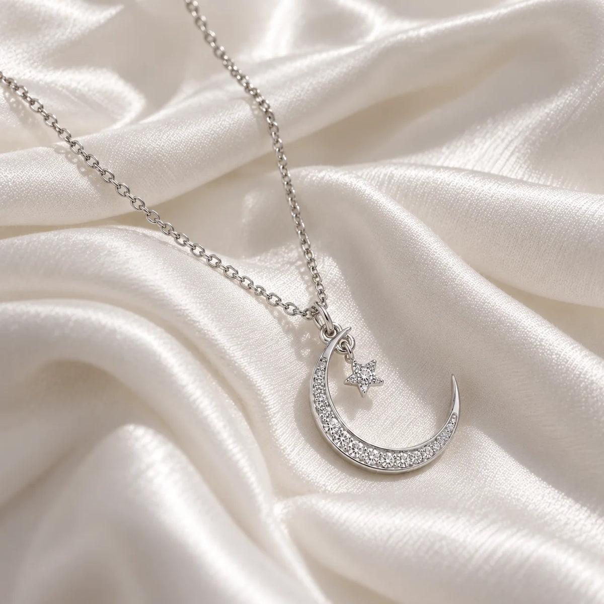 Moon_necklace_in_sterling_silver_with_a_small_star_charm_at_side_angle_view_on_soft_fabric_background