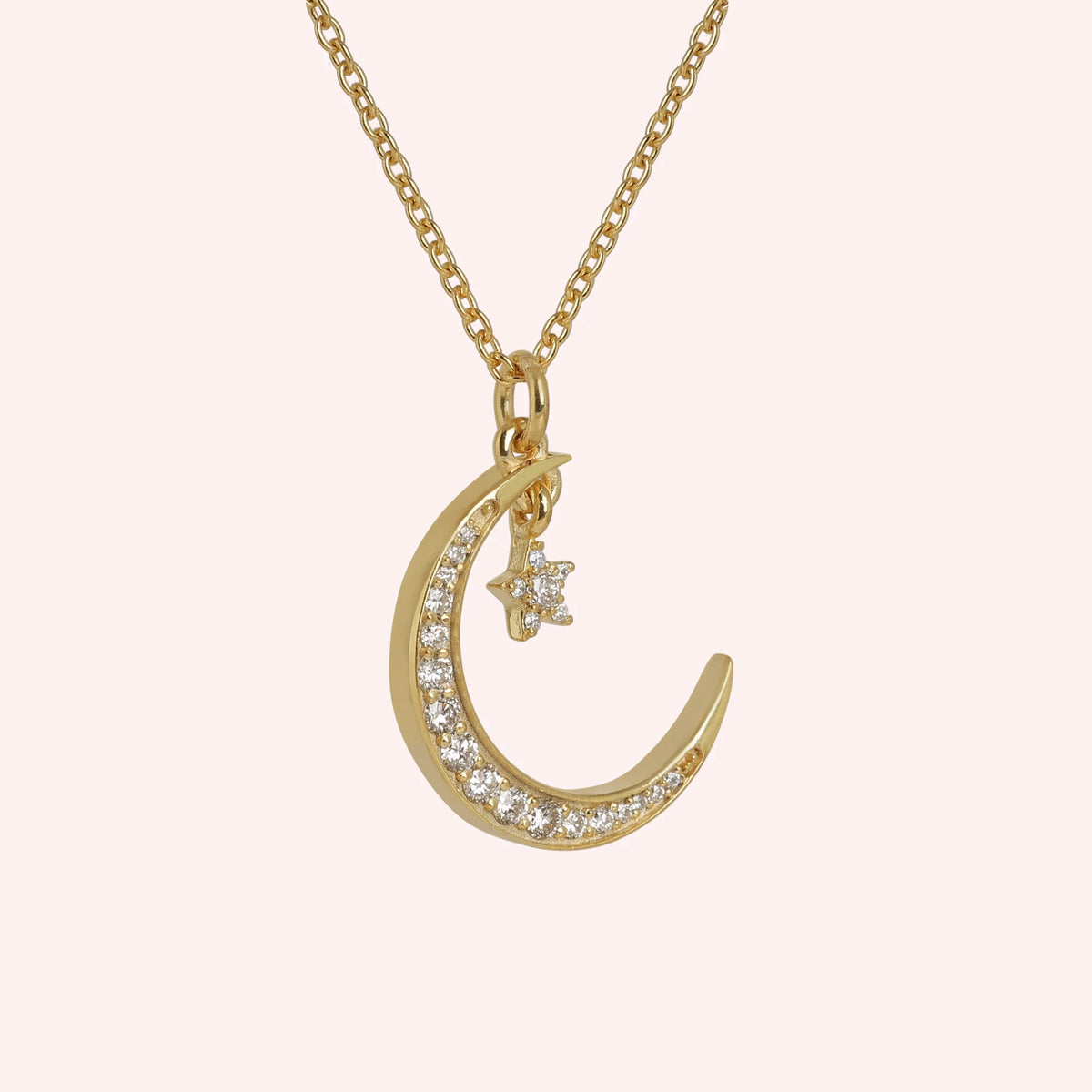 Moon_necklace_in_gold_plated_silver_with_a_small_star_charm_at_slight_angle_view_on_solid_pink_background