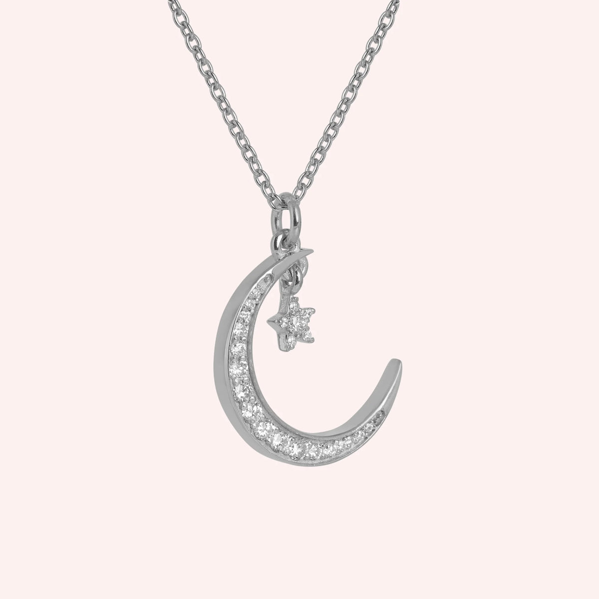 Moon_necklace_in_sterling_silver_with_a_small_star_charm_at_side_angle_view_on_solid_pink_background