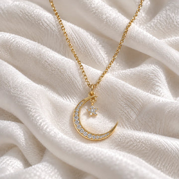 Moon_necklace_in_gold_plated_silver_with_a_small_star_charm_at_front_angle_view_on_soft_fabric_background