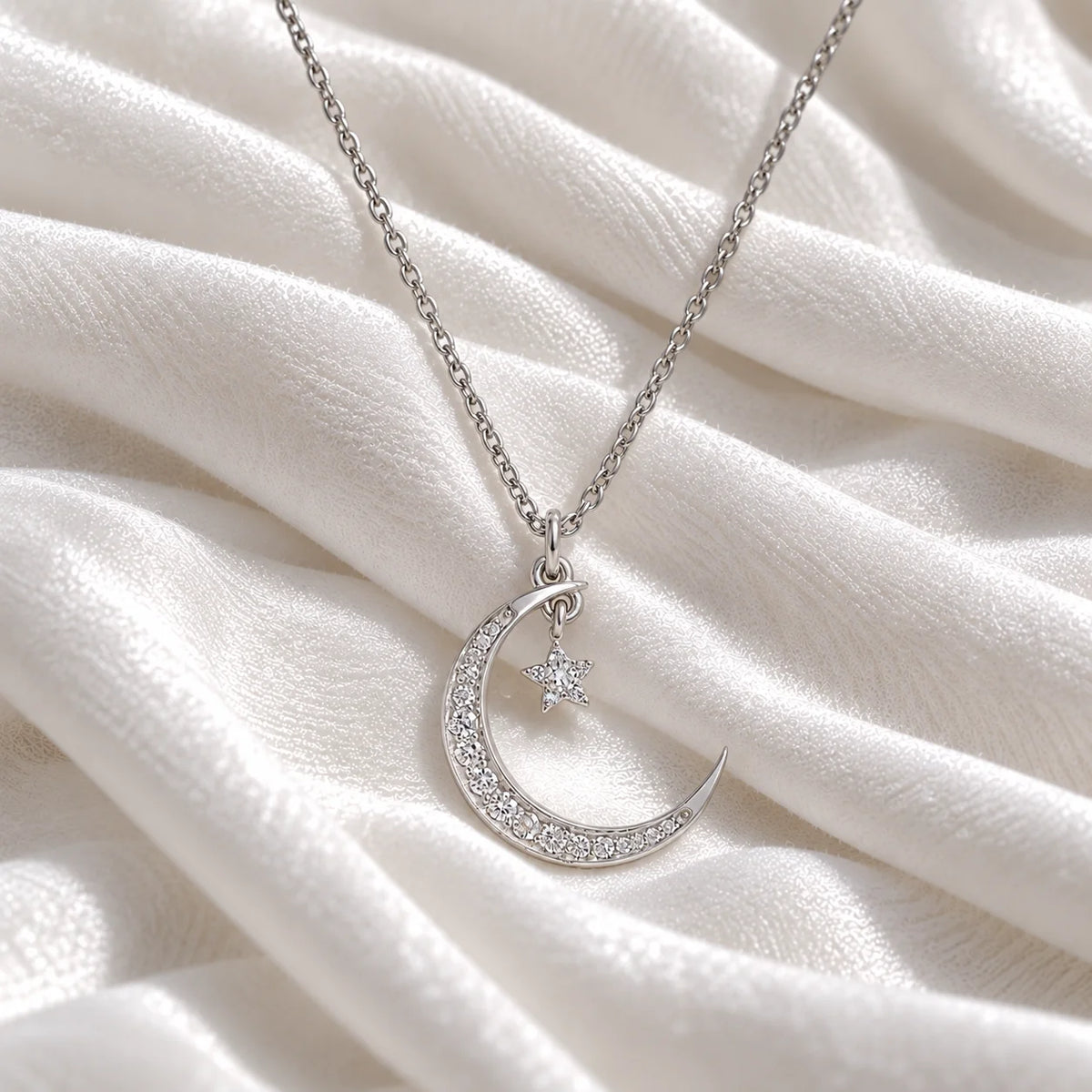 Moon_necklace_in_sterling_silver_with_a_small_star_charm_at_front_angle_view_on_soft_fabric_background
