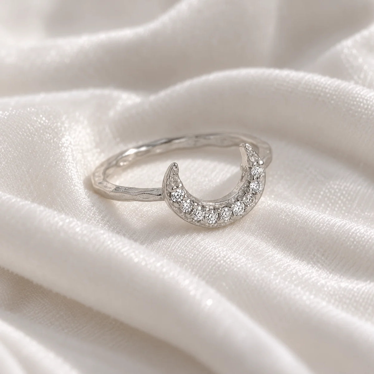Moon_ring_in_sterling_silver_in_a_crescent_moon_design_with_CZ_stones_at_side_angle_view_on_soft_fabric_background