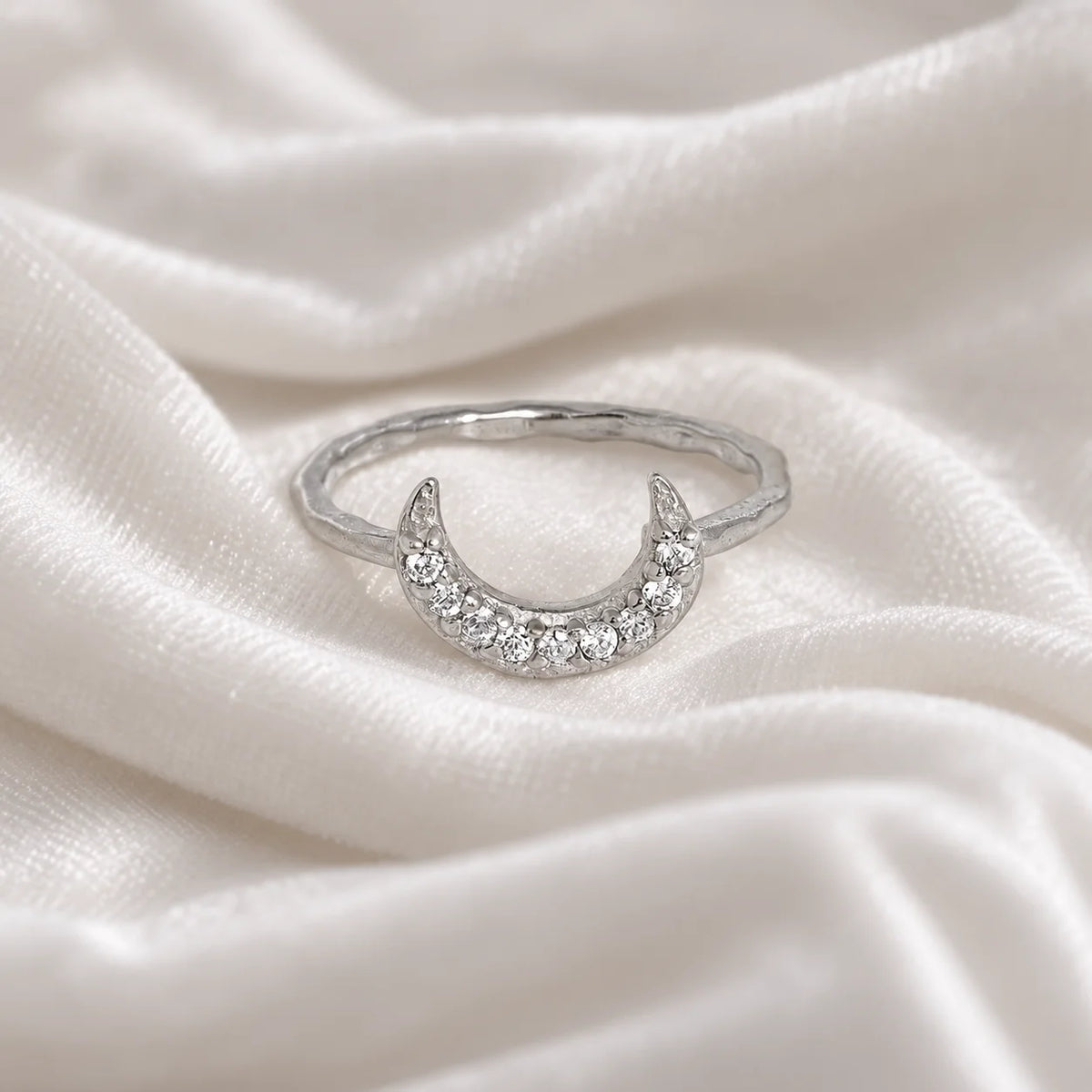 Moon_ring_in_sterling_silver_in_a_crescent_moon_design_with_CZ_stones_at_front_angle_view_on_soft_fabric_background
