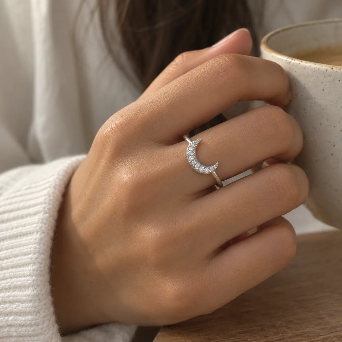 Moon_ring_in_sterling_silver_in_a_crescent_moon_design_with_CZ_stones_at_front_angle_view_worn_by_a_model