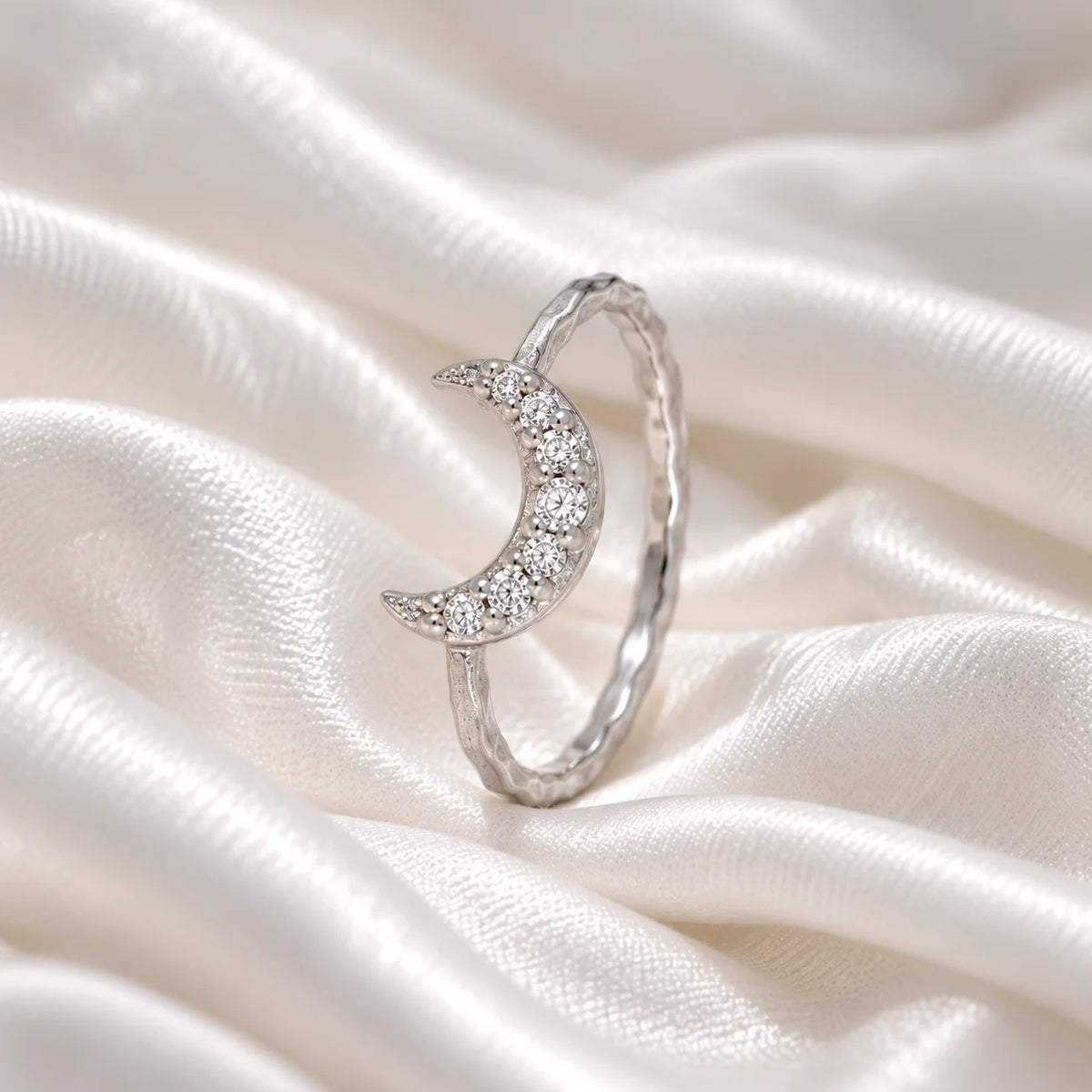 Moon_ring_in_sterling_silver_with_a_crescent_moon_design_at_side_angle_view_on_soft_fabric_background