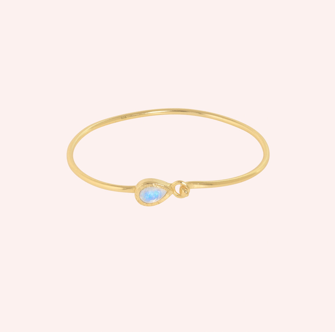 Moonstone_bracelet_in_gold_plated_silver_with_teardrop_moonstone_at_front_angle_view_on_solid_pink_background