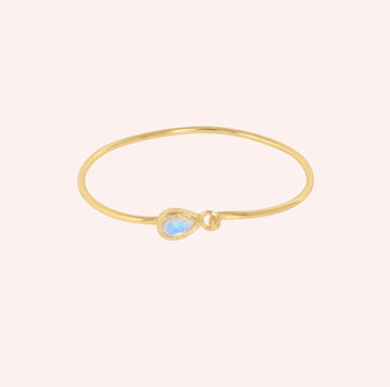 Moonstone_bracelet_in_gold_plated_silver_with_teardrop_moonstone_at_front_angle_view_on_solid_pink_background
