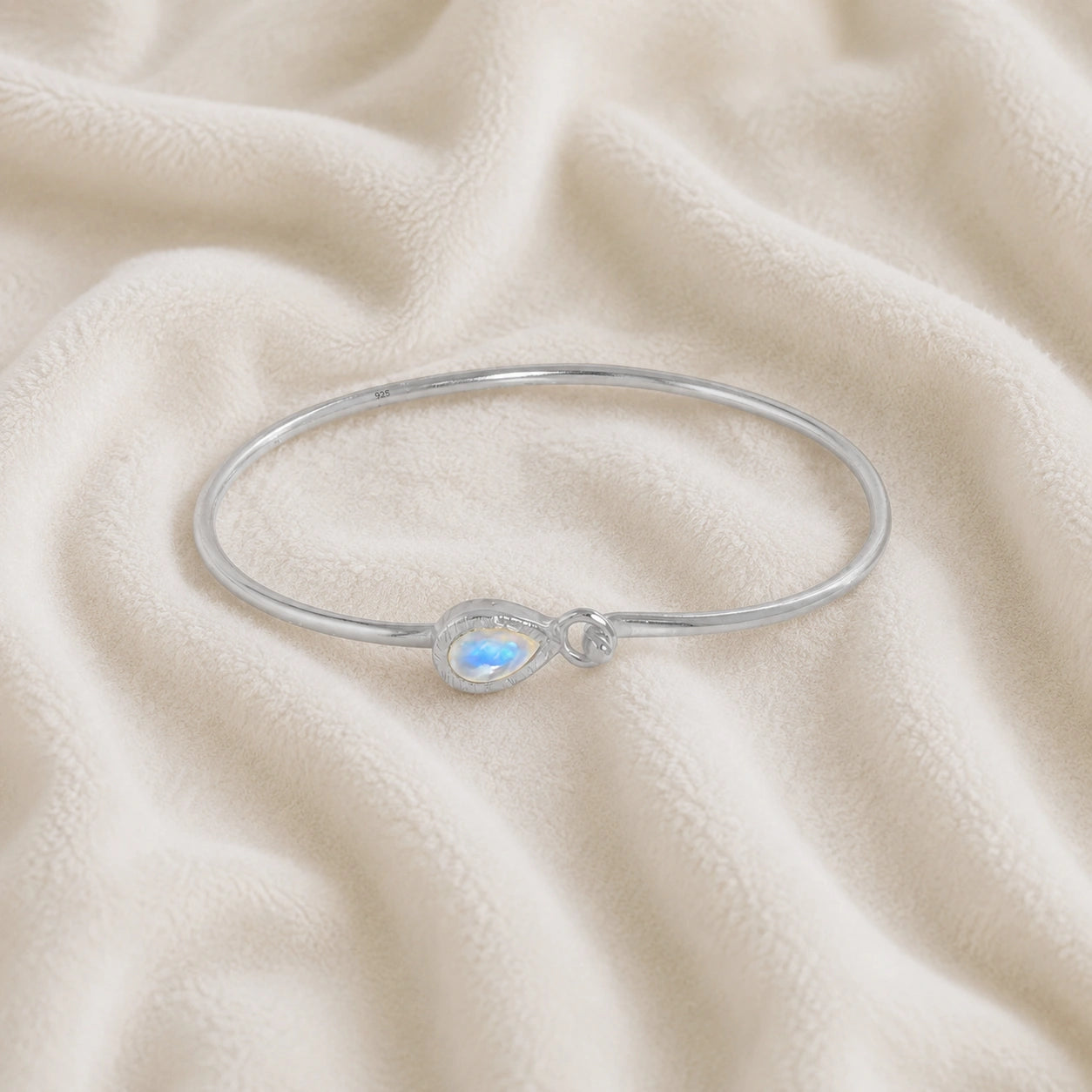 Moonstone_bracelet_in_sterling_silver_with_teardrop_moonstone_at_front_angle_view_on_soft_fabric_background