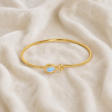 Moonstone_bracelet_in_gold_plated_silver_with_teardrop_moonstone_at_front_angle_view_on_soft_fabric_background