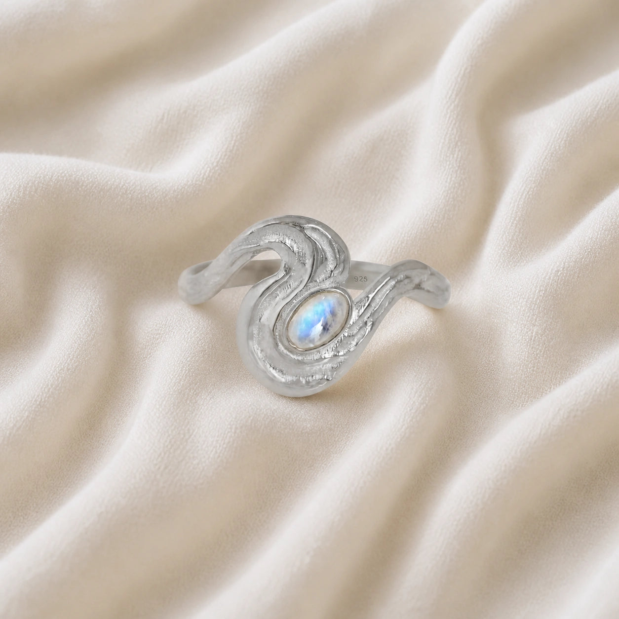 Moonstone_designer_ring_in_sterling_silver_with_moonstone_and_wave_band_shown_at_front_angle_view_on_soft_fabric_background