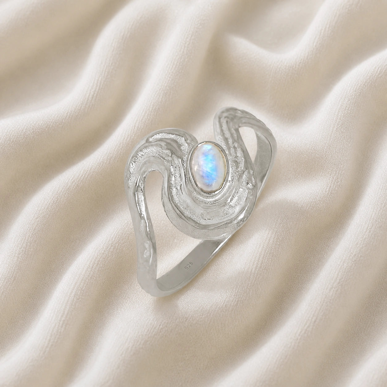 Moonstone_designer_ring_in_sterling_silver_with_moonstone_and_wave_band_shown_slightly_tilted_soft_fabric_background