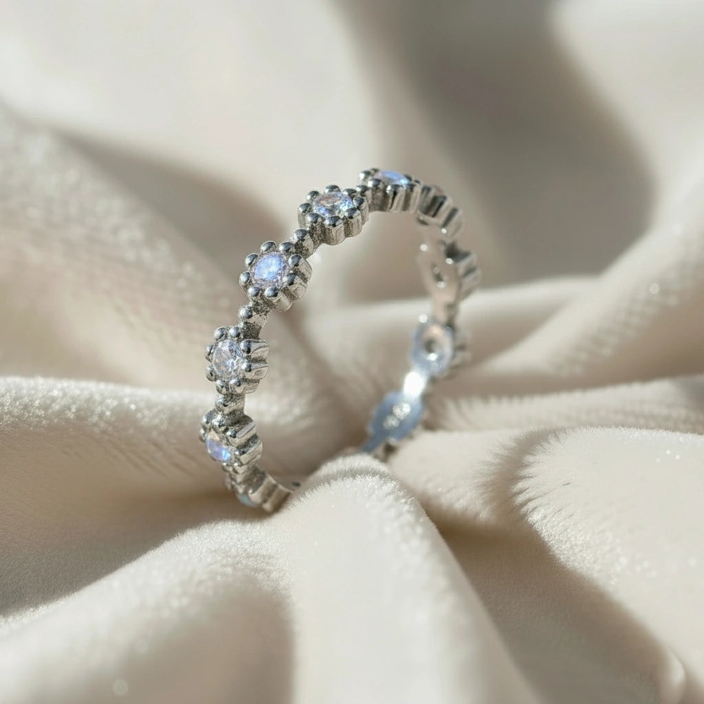 Sterling silver moonstone ring featuring flower settings with round gems captured at a higher angle on an off-white velvet fabric.