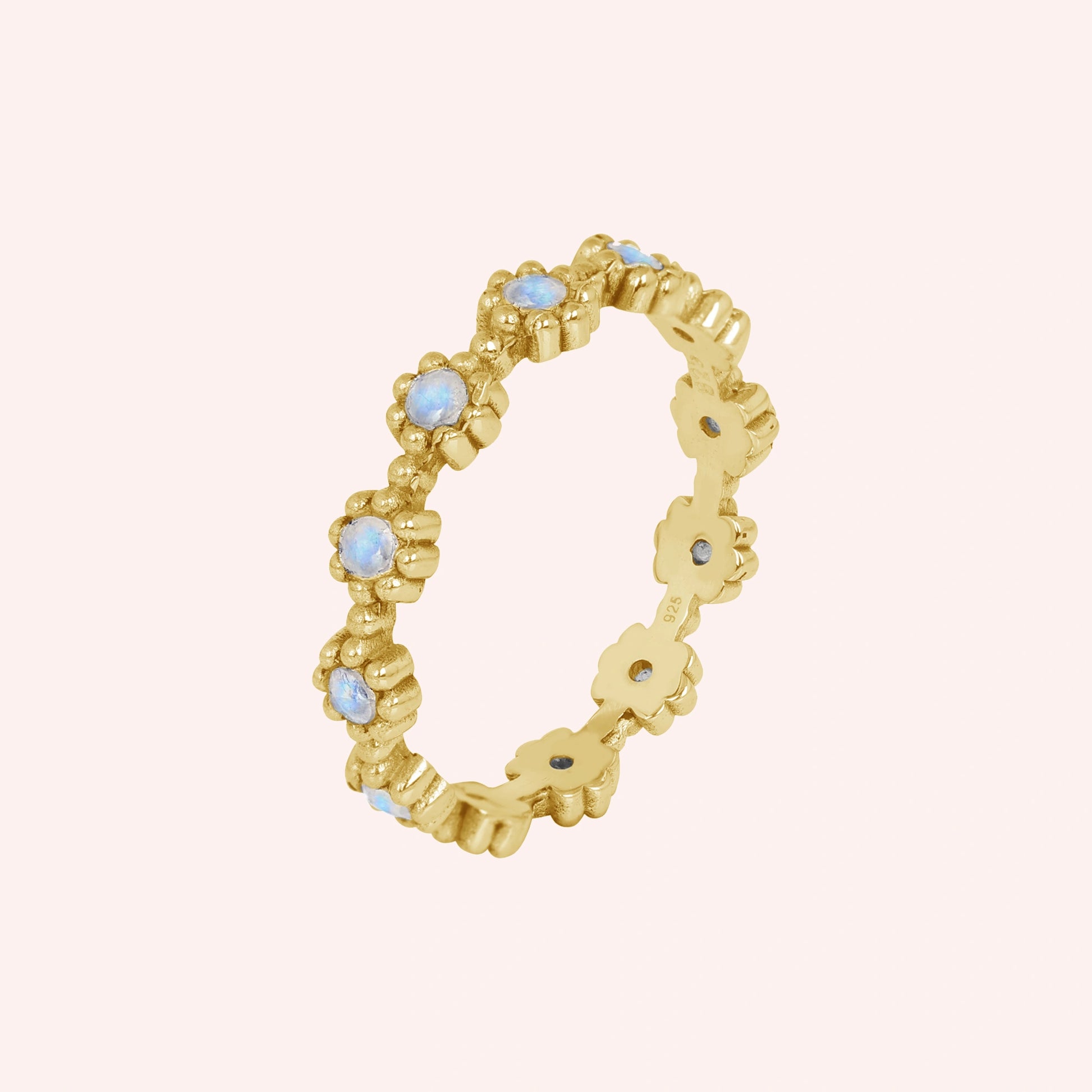 Gold-plated flower-designed moonstone ring full eternity band displaying small iridescent gems angled on a simple pink background.