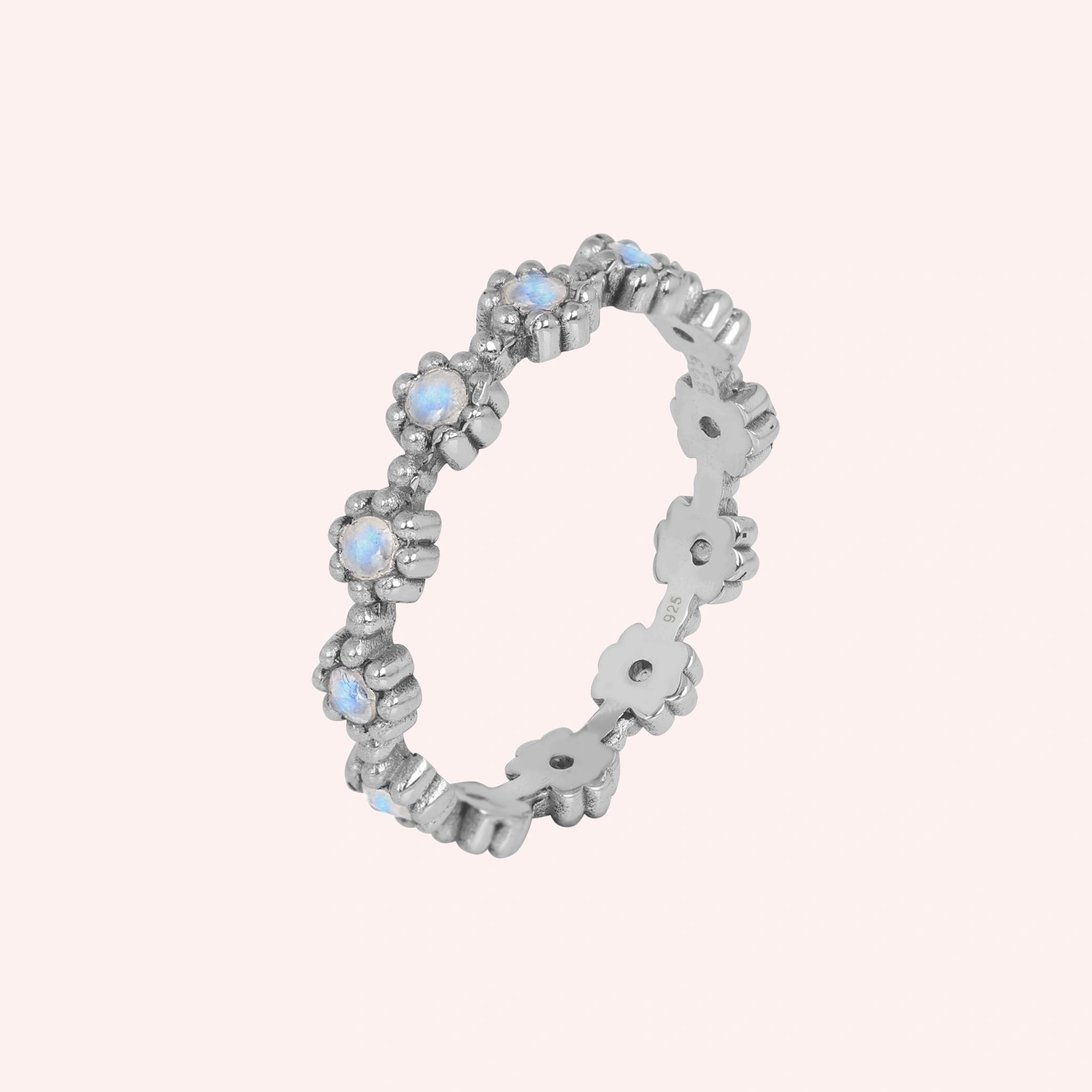 Angled sterling silver moonstone ring full eternity band featuring small flower settings holding iridescent round gems on a pink background.