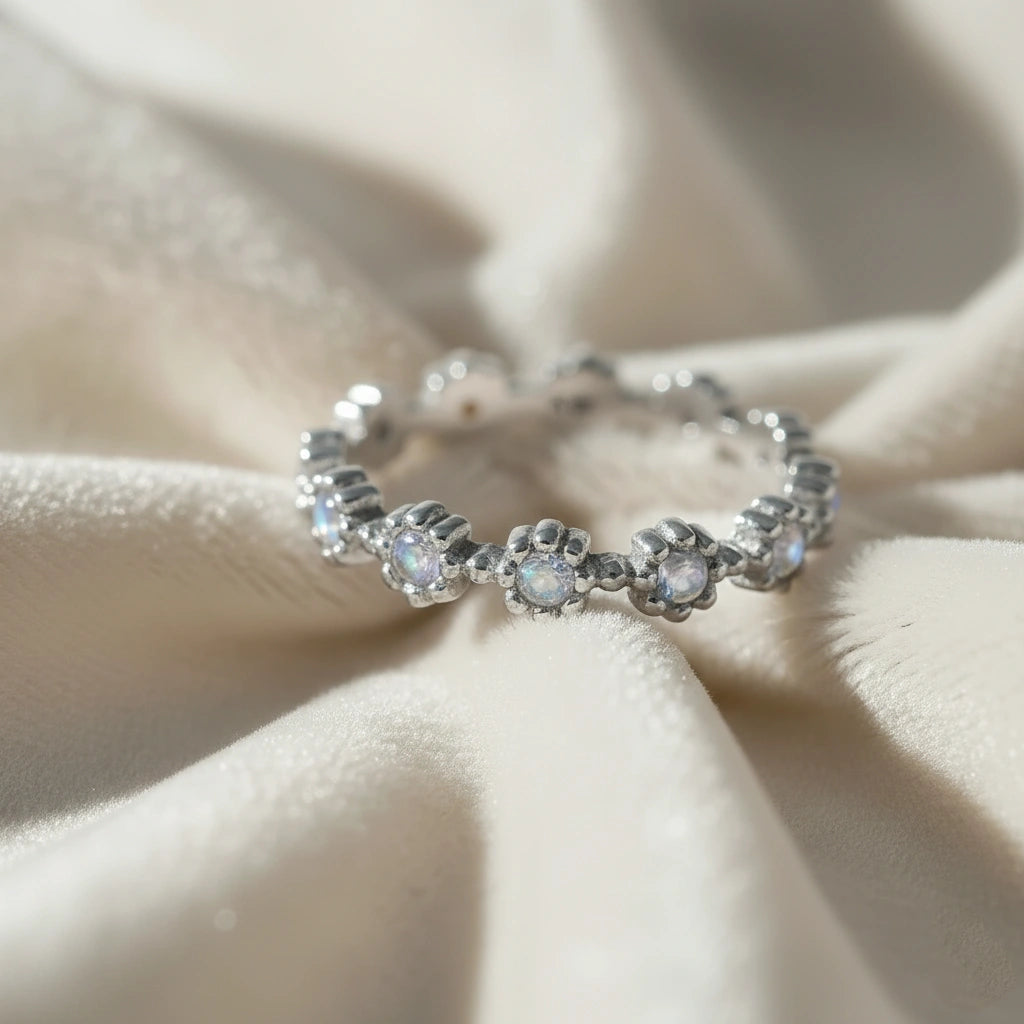 Angled sterling silver moonstone ring full eternity band featuring flower settings and round gems on off-white velvet cloth.