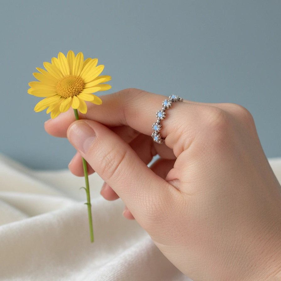 Sterling silver moonstone ring featuring flower settings with round gems captured at a higher angle on an off-white velvet fabric.