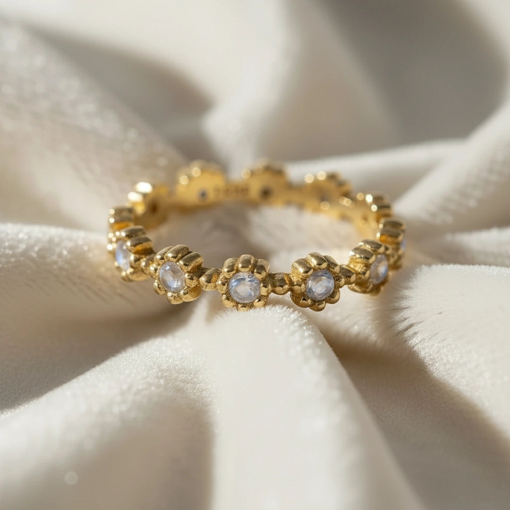 Gold-plated flower-designed moonstone ring full eternity band with round gems on the central folds of off-white velvet fabric.