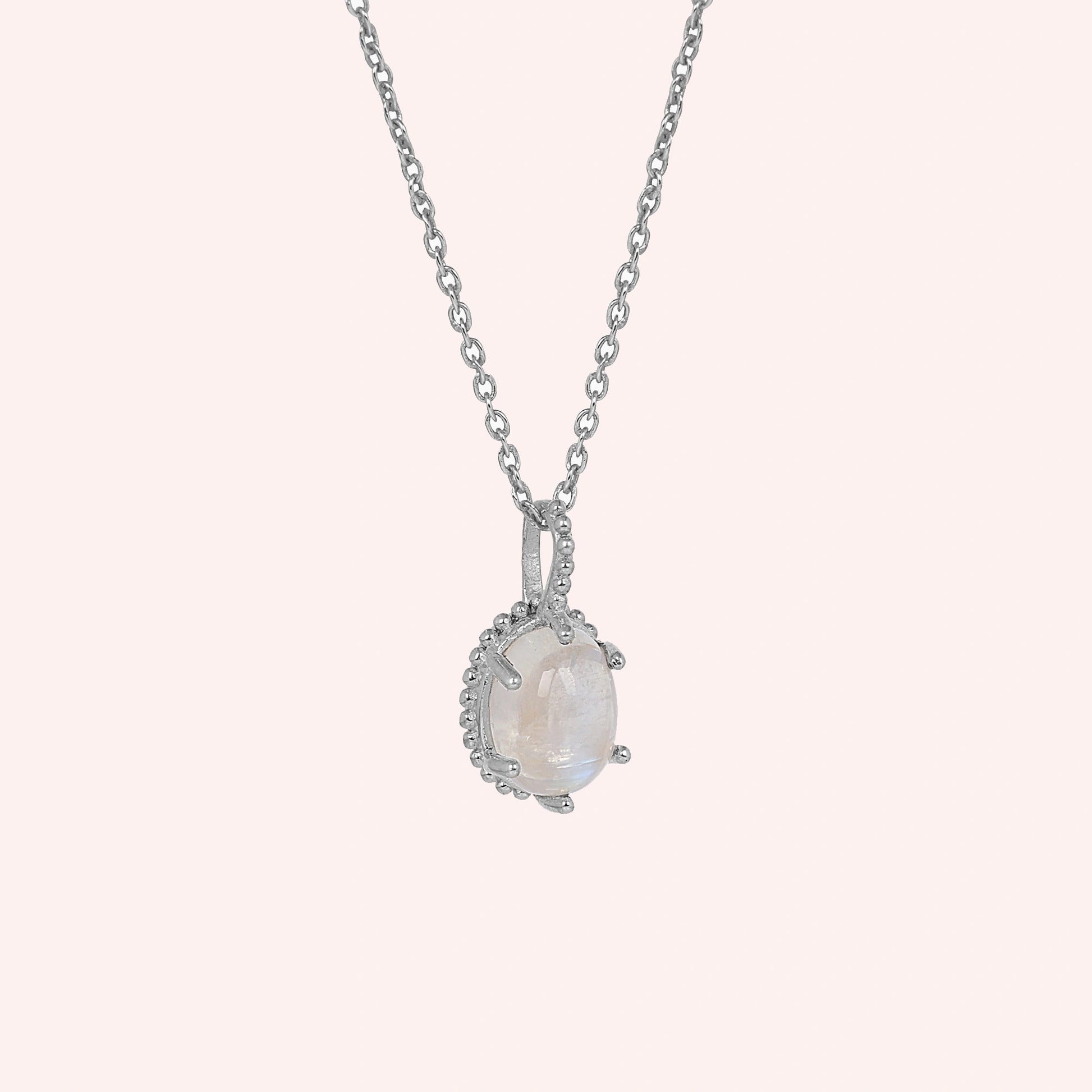 Moonstone_necklace_in_sterling_silver_and_glowing_moonstone_in_slightly_angled_view_on_solid_pink_background