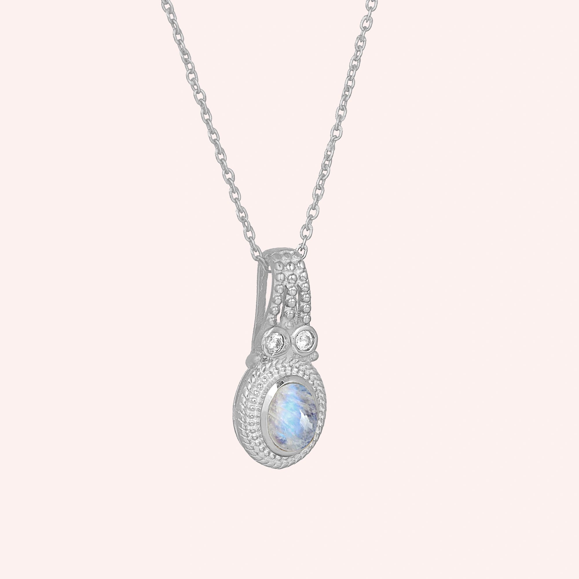 Moonstone_pendant_in_sterling_silver_with_oval_moonstone_and_CZ_stones_shown_in_slightly_angled_on_solid_pink_background