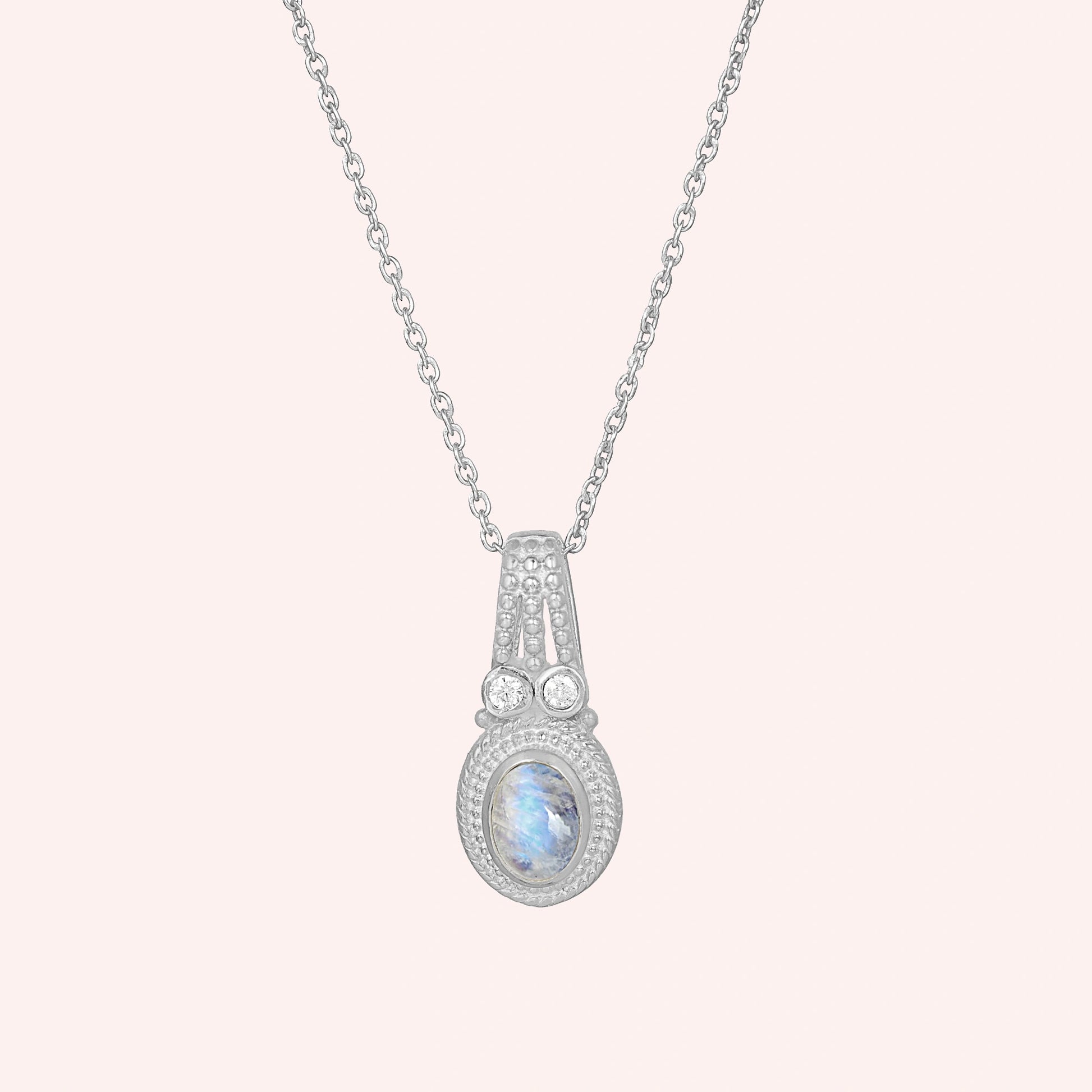 Moonstone_pendant_in_sterling_silver_with_oval_moonstone_and_CZ_stones_shown_in_front_angle_on_solid_pink_background