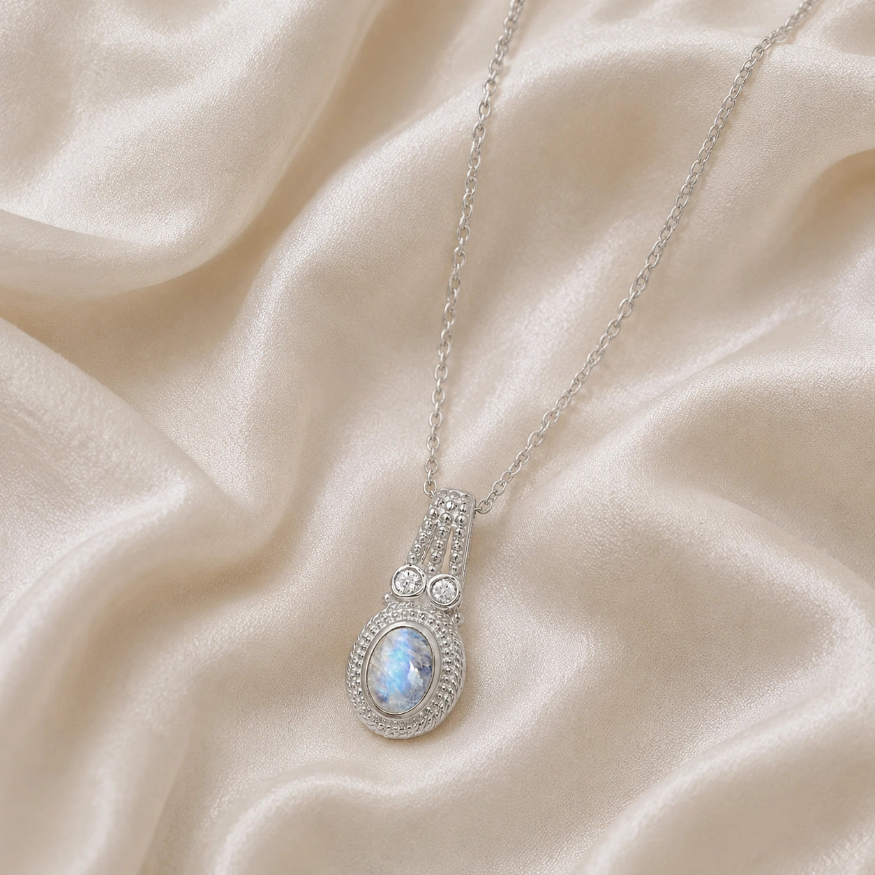 Moonstone_pendant_in_sterling_silver_with_oval_moonstone_and_CZ_stones_shown_in_slightly_angled_on_soft_fabric_background