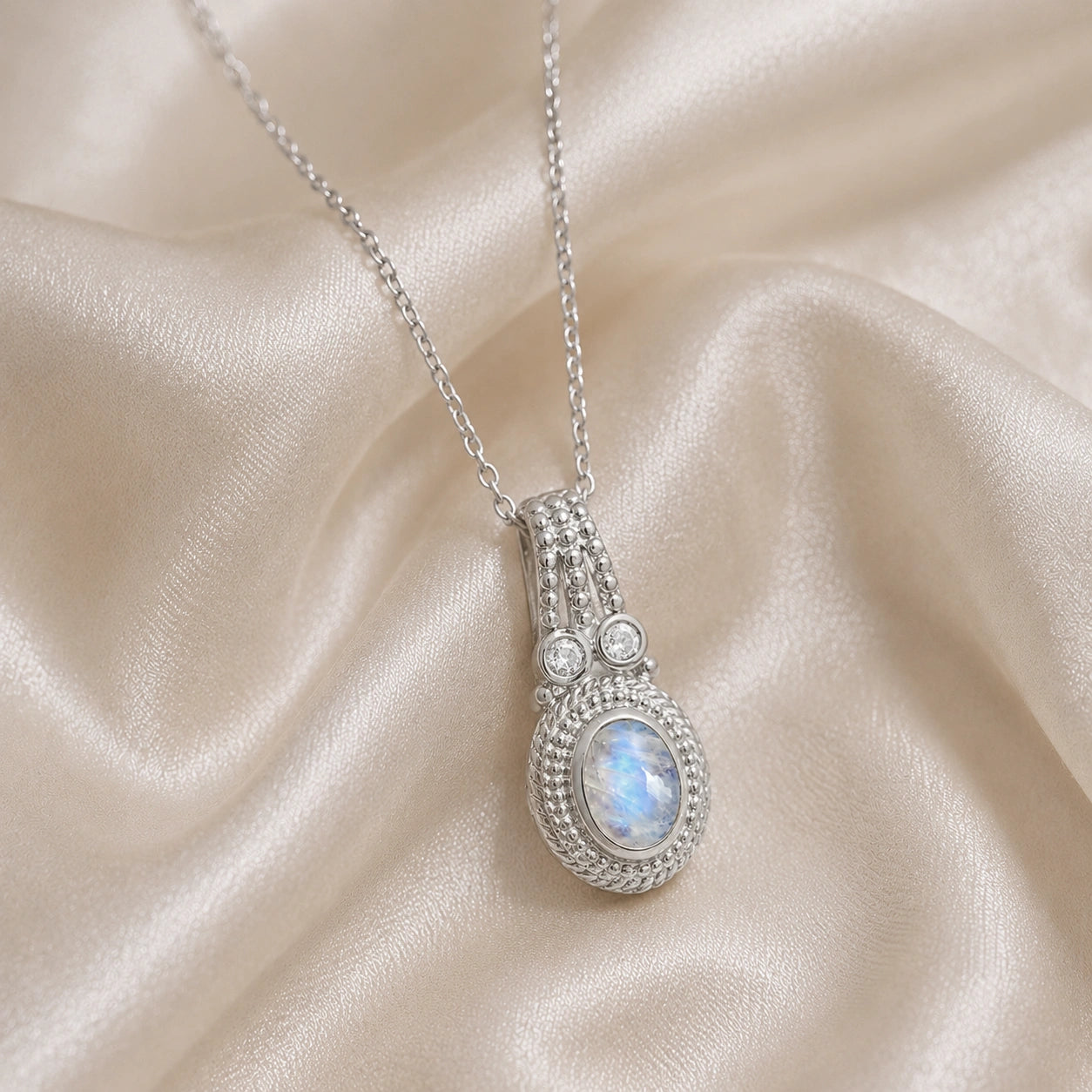 Moonstone_pendant_in_sterling_silver_with_oval_moonstone_and_CZ_stones_shown_in_front_angle_on_soft_fabric_background