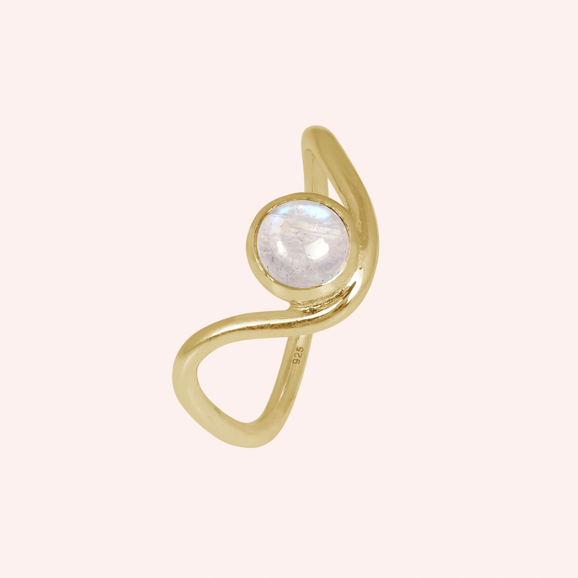 A gold plated moonstone ring with a round moonstone and a wave ring band at a tilted angle over a light pink plain background