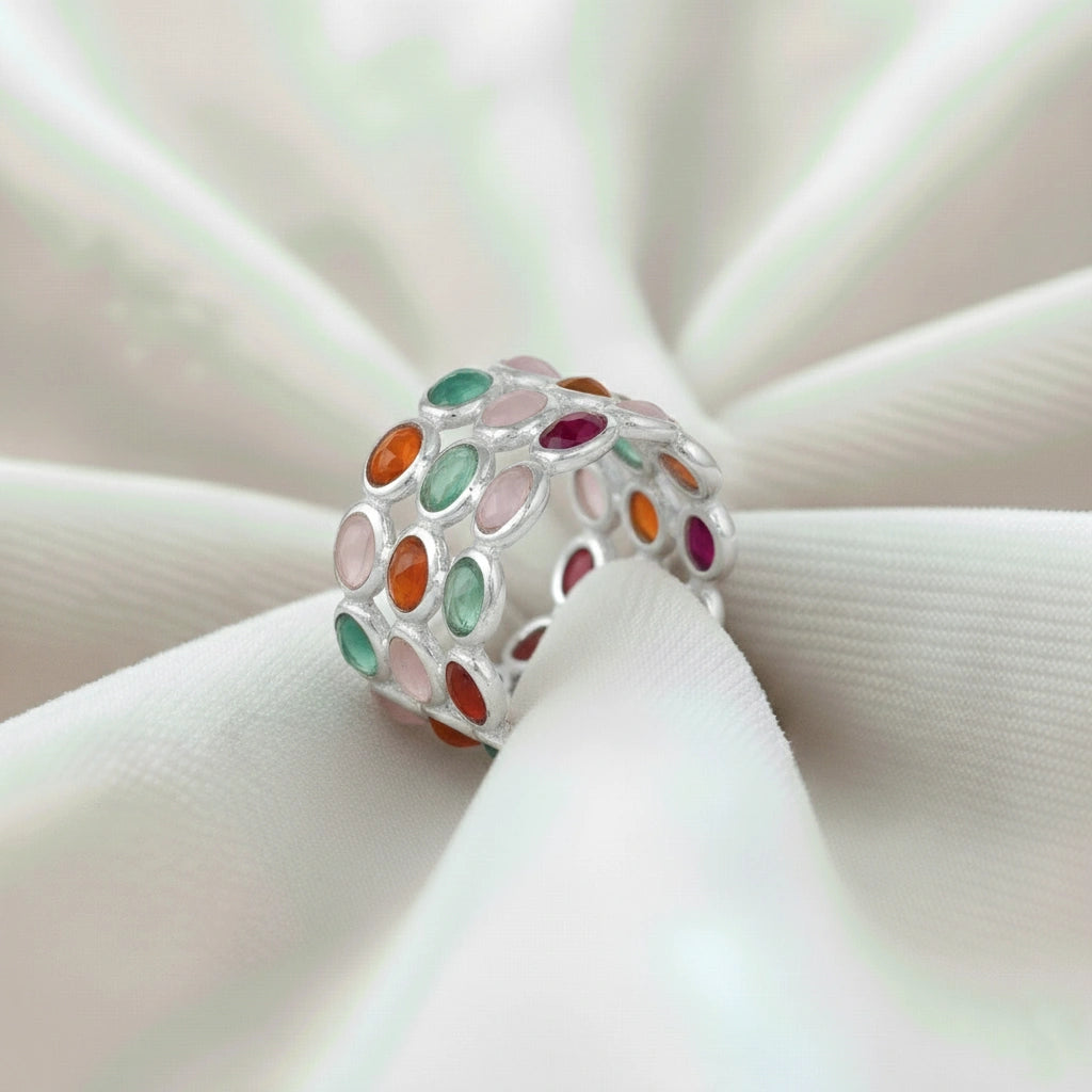 Silver multi stone ring with three bands of oval rose quartz carnelian green onyx stones on a wrinkled white velvet cloth.