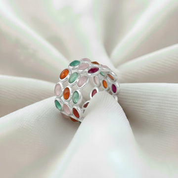 Silver multi stone ring with three bands of oval rose quartz carnelian green onyx stones on a wrinkled white velvet cloth.