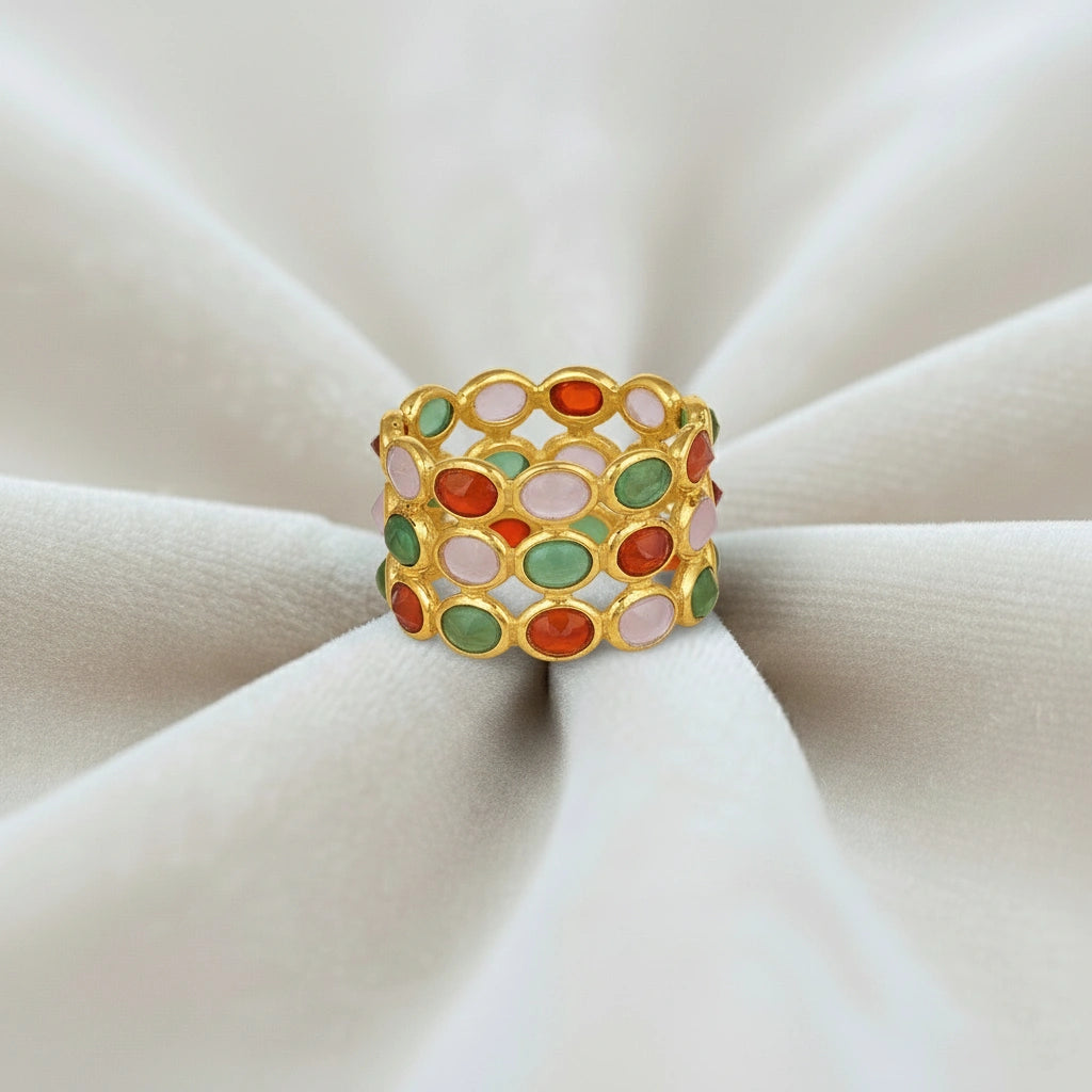 Silver multi stone ring with a gold finish band of oval carnelian rose quartz green onyx gems on a wrinkled off white velvet fabric.