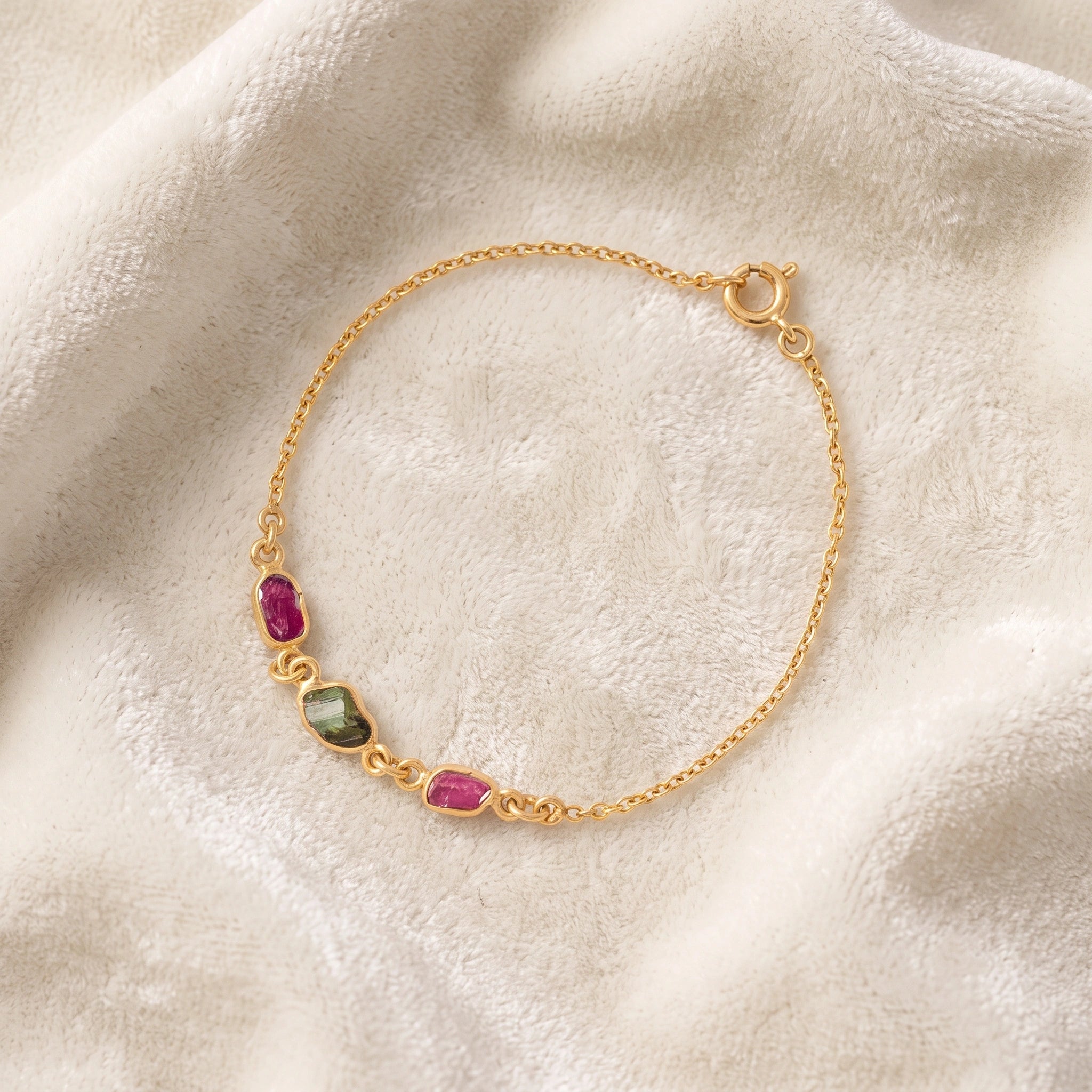Multi_tourmaline_bracelet_in_gold_plated_silver_with_pink_and_green_tourmaline_at_slight_angle_view_on_soft_fabric_backgrou
