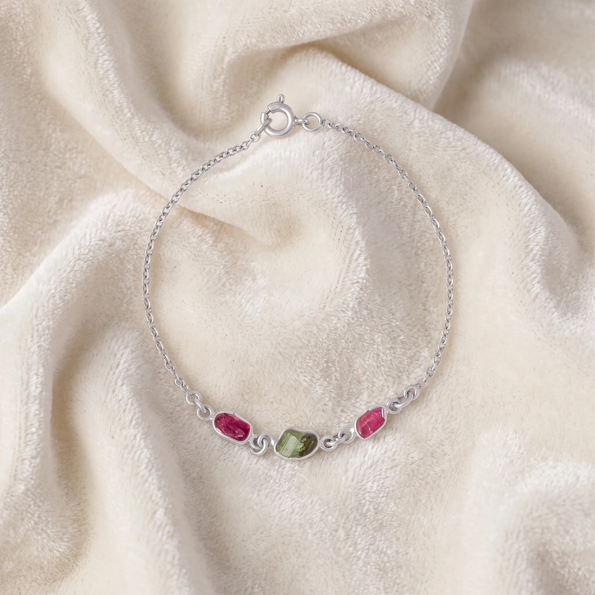 Multi_tourmaline_bracelet_in_sterling_silver_with_pink_and_green_tourmaline_at_front_angle_view_on_soft_fabric_backgrou