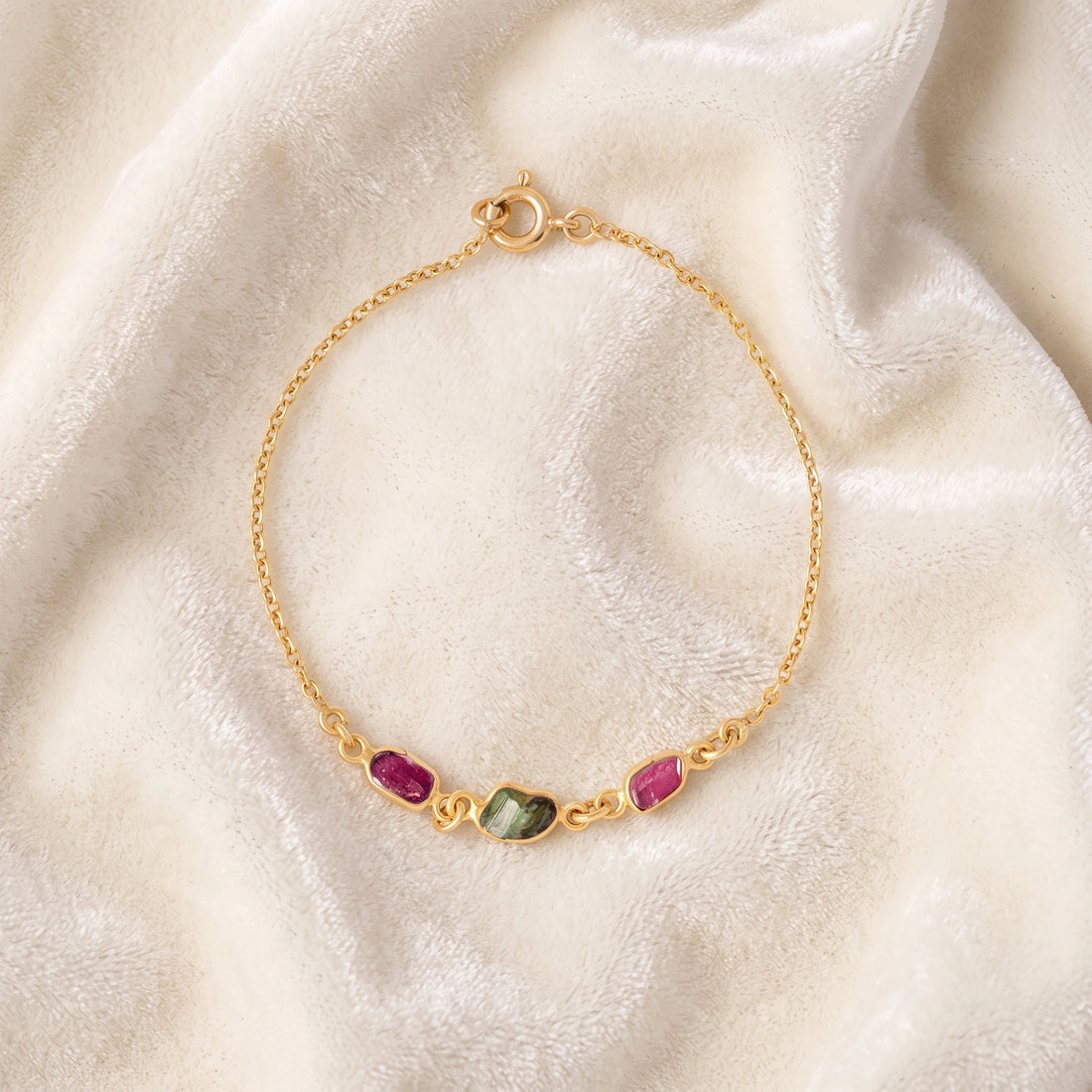 Multi_tourmaline_bracelet_in_gold_plated_silver_with_pink_and_green_tourmaline_at_front_angle_view_on_soft_fabric_backgrou