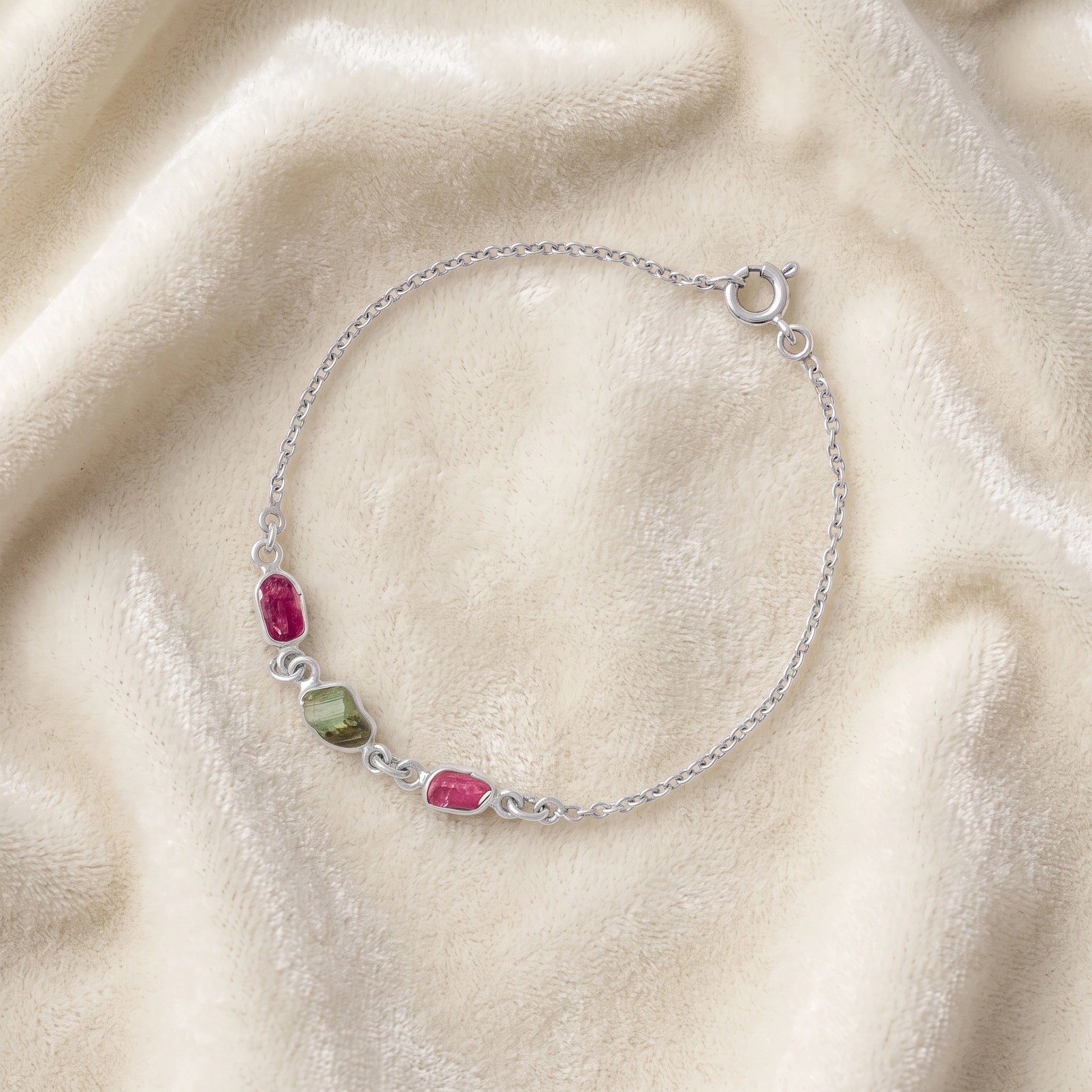 Multi_tourmaline_bracelet_in_sterling_silver_with_pink_and_green_tourmaline_at_slight_angle_view_on_soft_fabric_backgrou