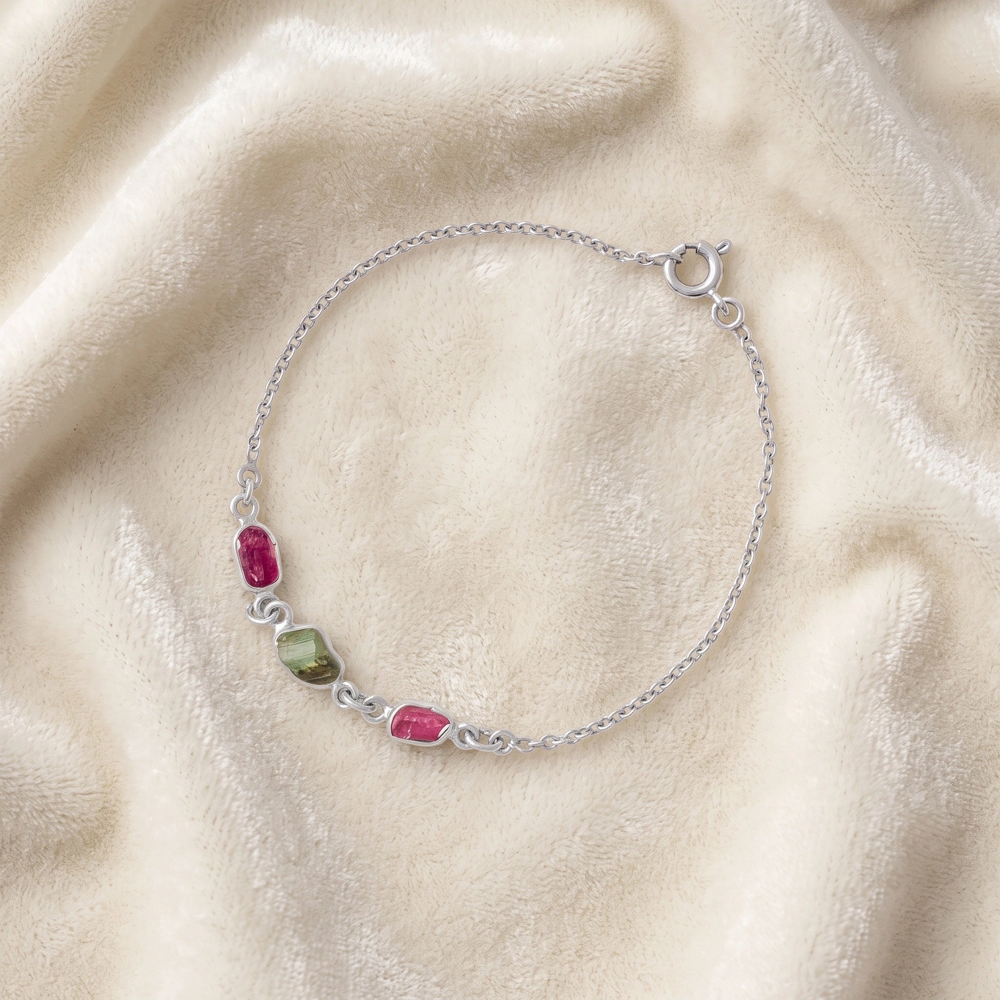 Multi_tourmaline_bracelet_in_sterling_silver_with_pink_and_green_tourmaline_at_slight_angle_view_on_soft_fabric_backgrou