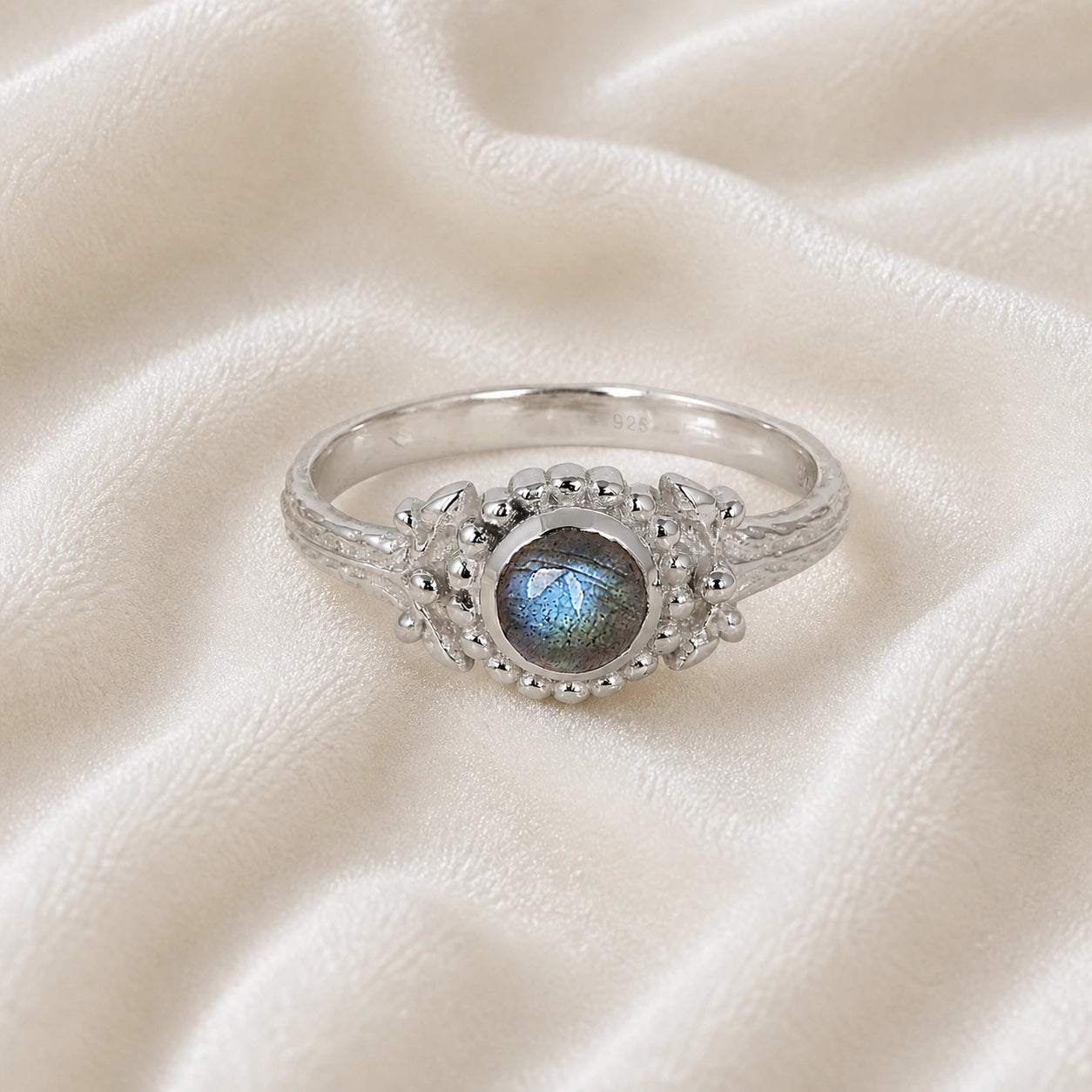 Natural_stone_ring_sterling_silver_with_round_labradorite_and_detailed_band_front_angle_view_on_soft_fabric_background