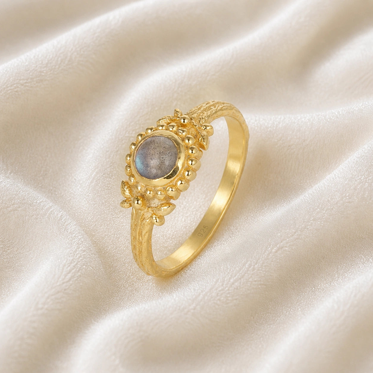 Natural_stone_ring_gold_plated_silver_with_round_labradorite_and_detailed_band_slightly_tilted_view_on_soft_fabric_background
