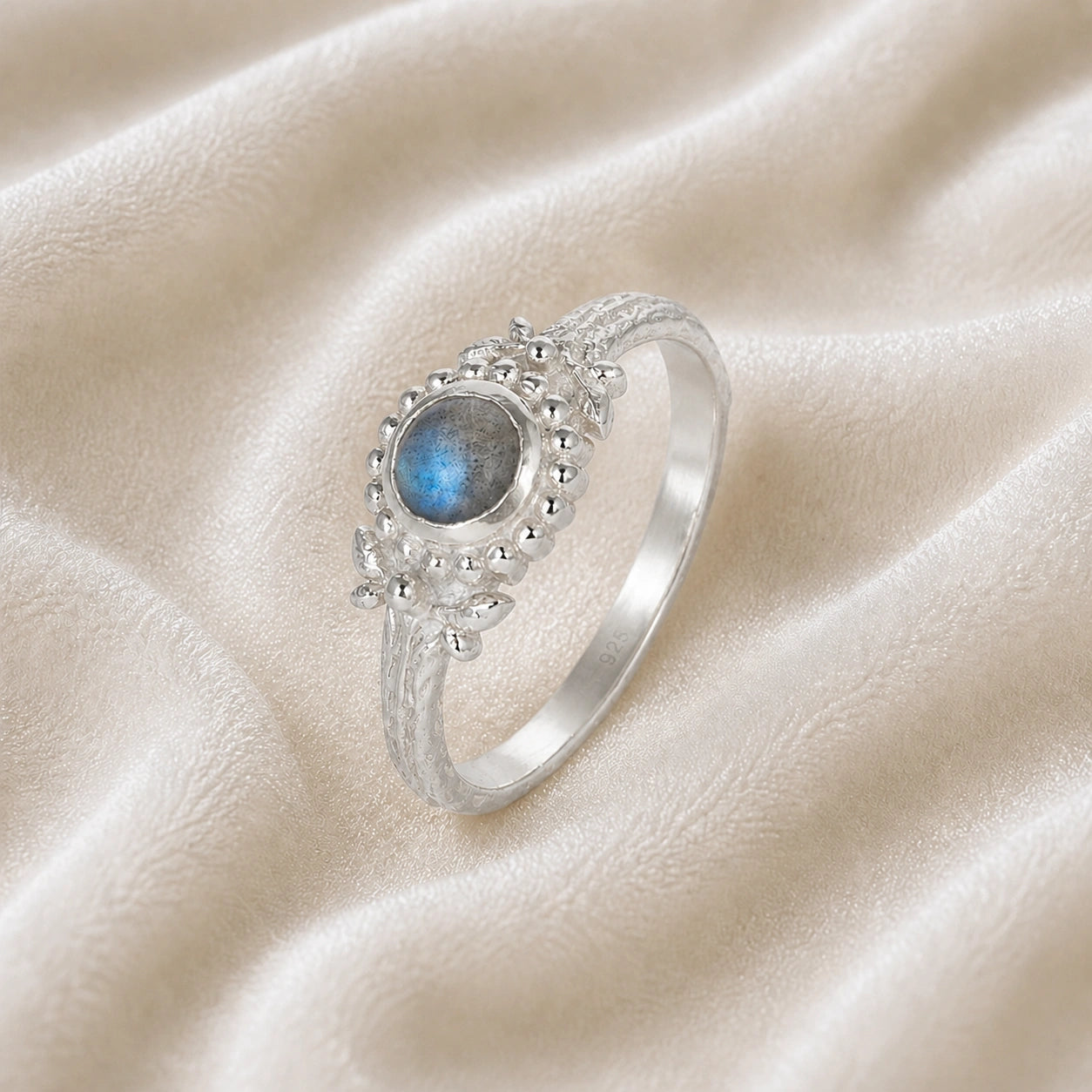 Natural_stone_ring_sterling_silver_with_round_labradorite_and_detailed_band_slightly_tilted_view_on_soft_fabric_background