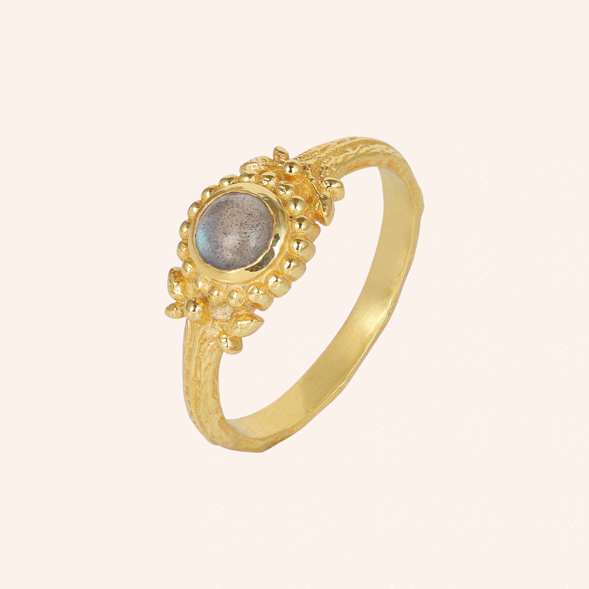 Natural_stone_ring_gold_plated_silver_with_round_labradorite_and_detailed_band_slightly_tilted_view_on_solid_pink_background
