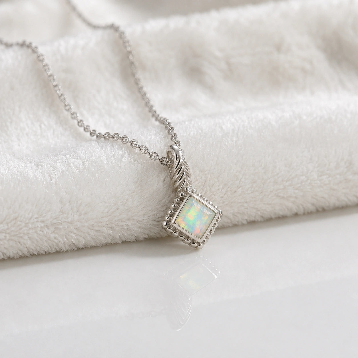 Birthstone_necklace_in_sterling_silver_with_square_cut_opal_pendant_in_slightly_angled_view_on_soft_white_fabric_background