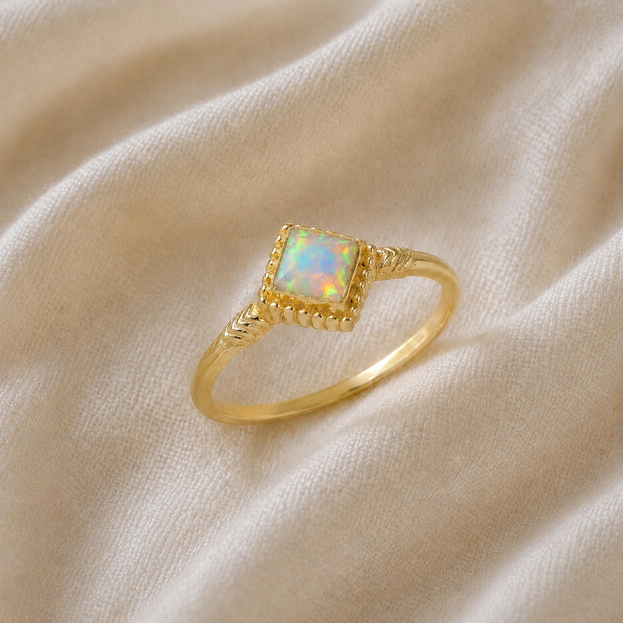 Princess_cut_ring_gold_plated_silver_with_square_opal_and_detailed_band_slightly_tilted_view_on_soft_fabric_background