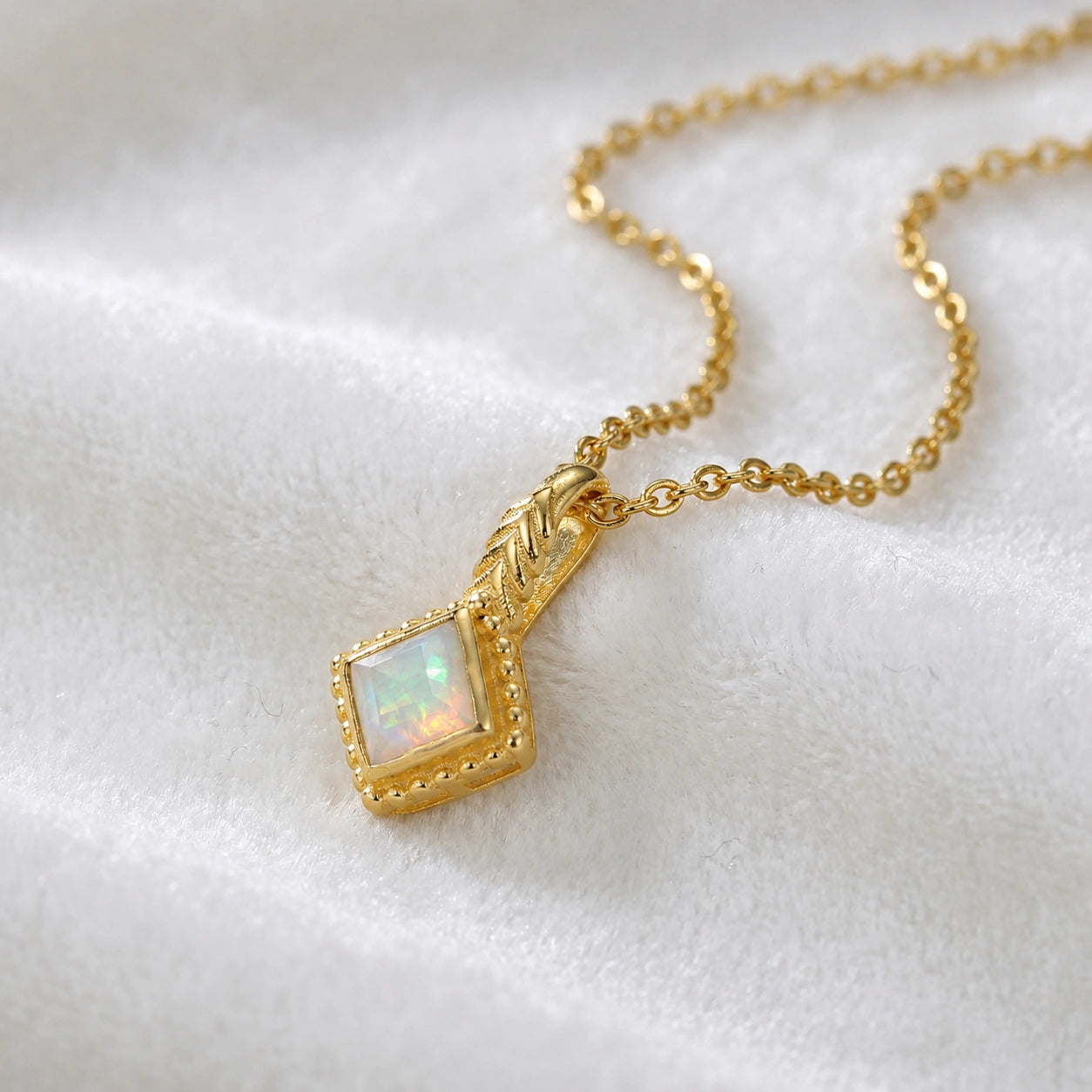 Birthstone_necklace_in_gold_plated_silver_with_square_cut_opal_pendant_in_slightly_angled_view_on_soft_white_fabric_background