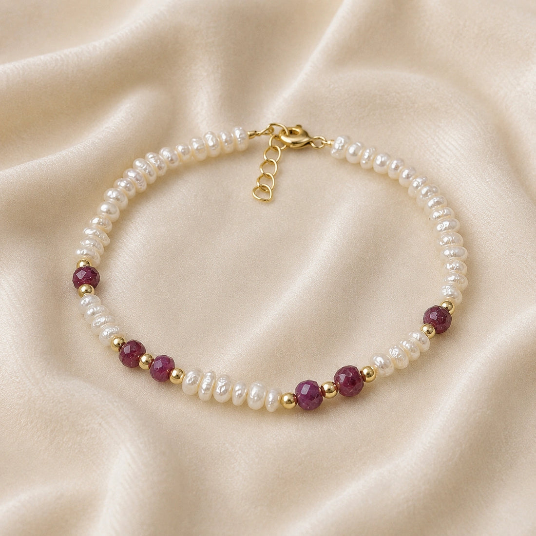 Pearl_bracelet_with_pearl_and_ruby_stones_in_gold_plated_silver_at_front_angle_view_on_soft_fabric_background