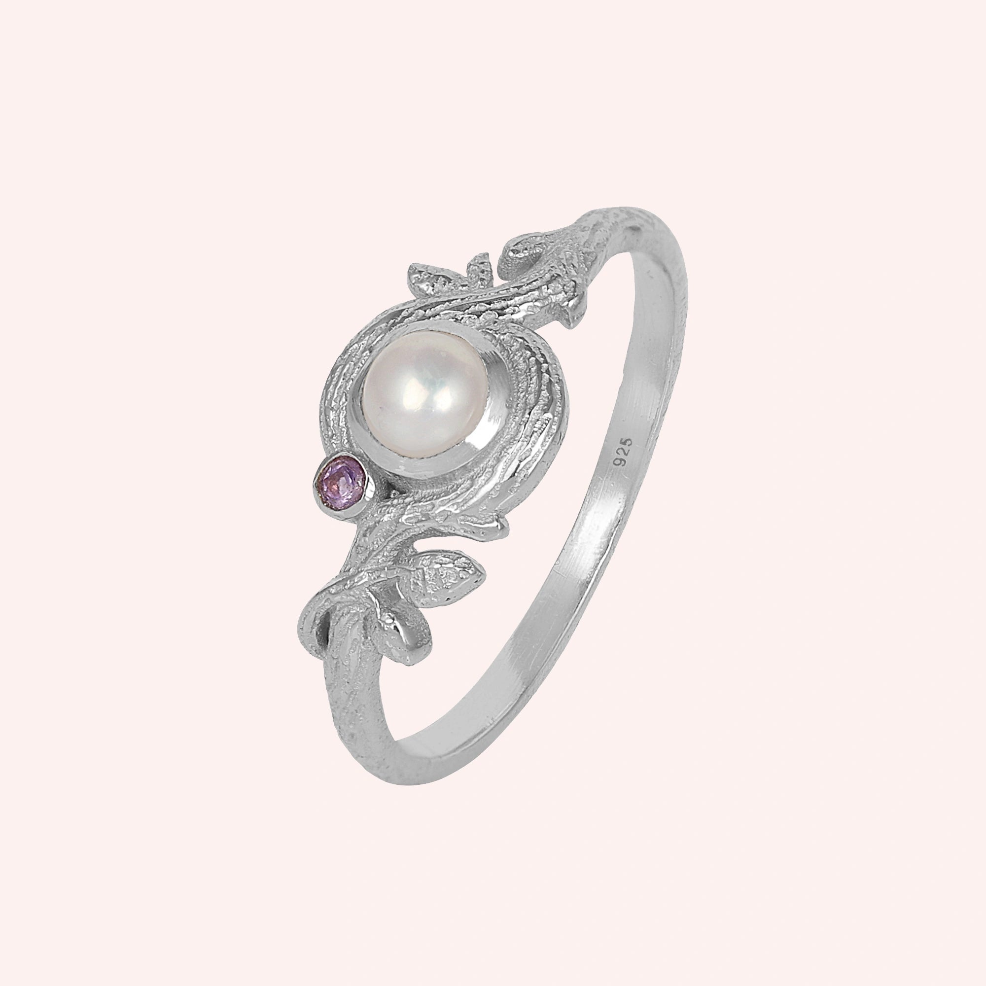 Pearl_ring_in_sterling_silver_with_pearl_and_amethyst_stones_in_a_floral_design_at_slight_angle_view_on_solid_pink_background