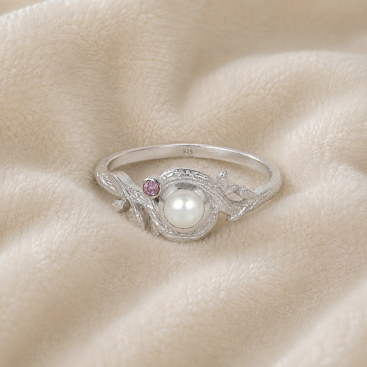 Pearl_ring_in_sterling_silver_with_pearl_and_amethyst_stones_in_a_floral_design_at_front_angle_view_on_soft_fabric_background
