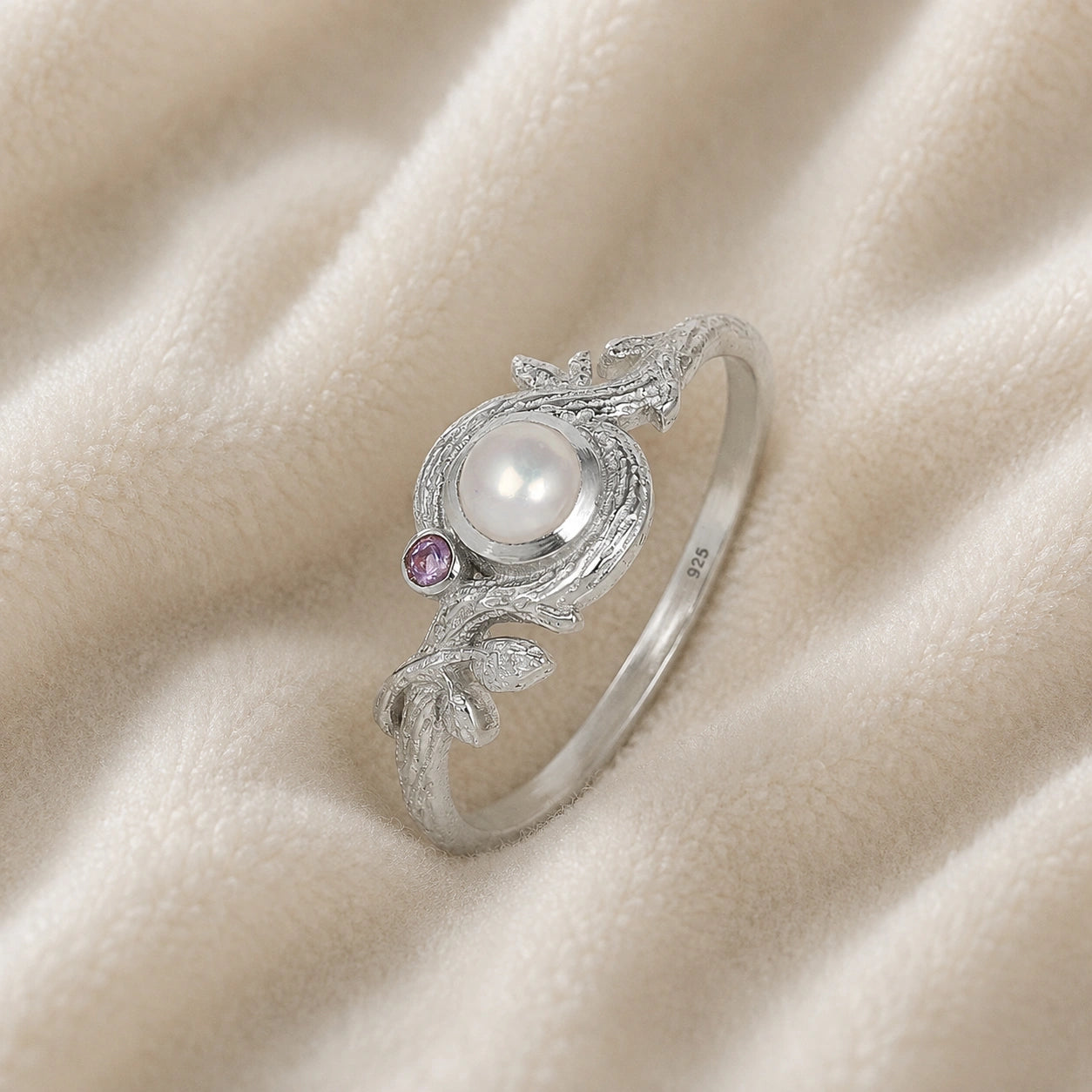 Pearl_ring_in_sterling_silver_with_pearl_and_amethyst_stones_in_a_floral_design_at_slight_angle_view_on_soft_fabric_background