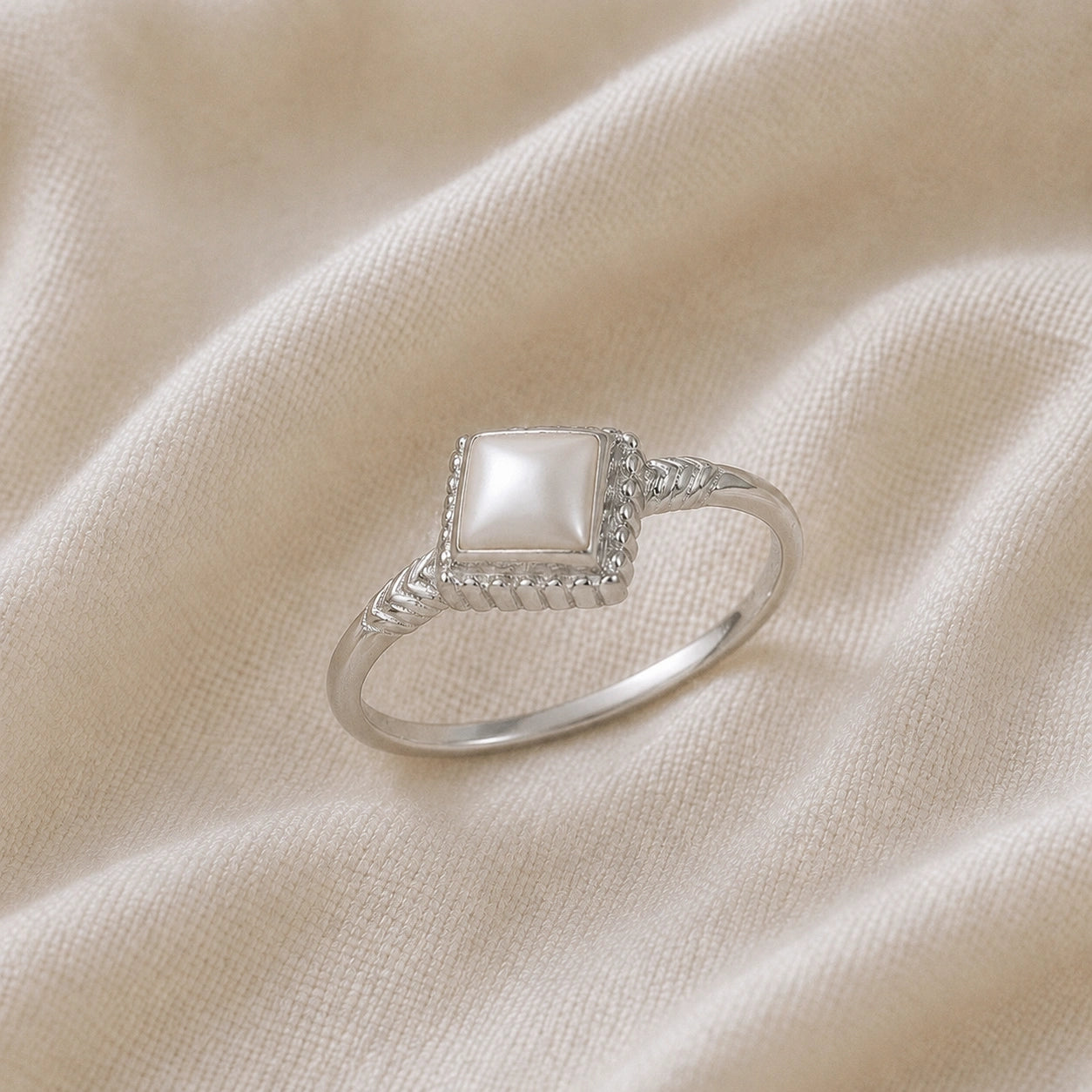 Princess_cut_ring_sterling_silver_with_square_pearl_and_detailed_band_slightly_tilted_view_on_soft_fabric_background