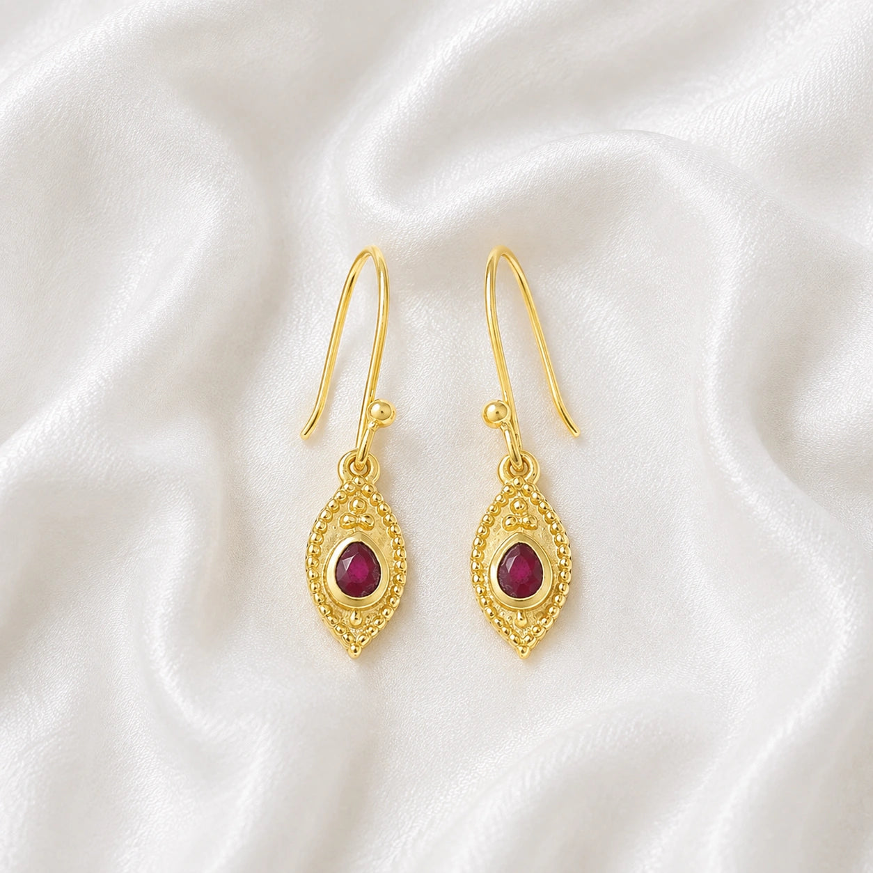 Pink_earrings_in_gold_plated_silver_with_pear_ruby_stones_at_front_angle_view_on_soft_fabric_background