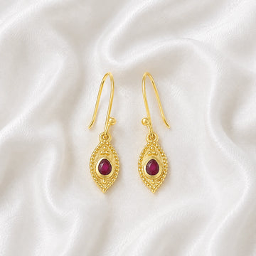 Pink_earrings_in_gold_plated_silver_with_pear_ruby_stones_at_front_angle_view_on_soft_fabric_background